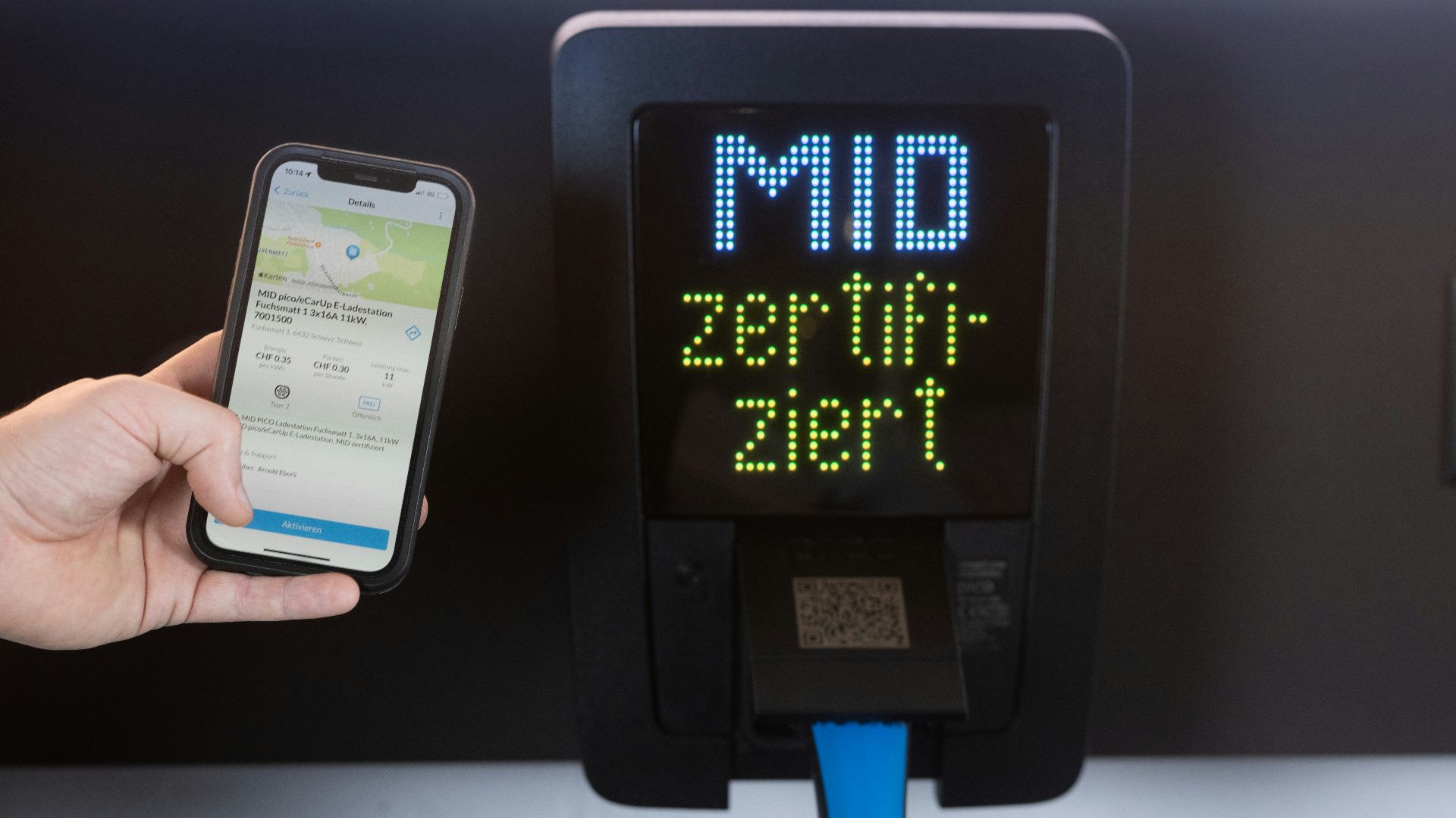 Hand holding smartphone next to ev charging station.