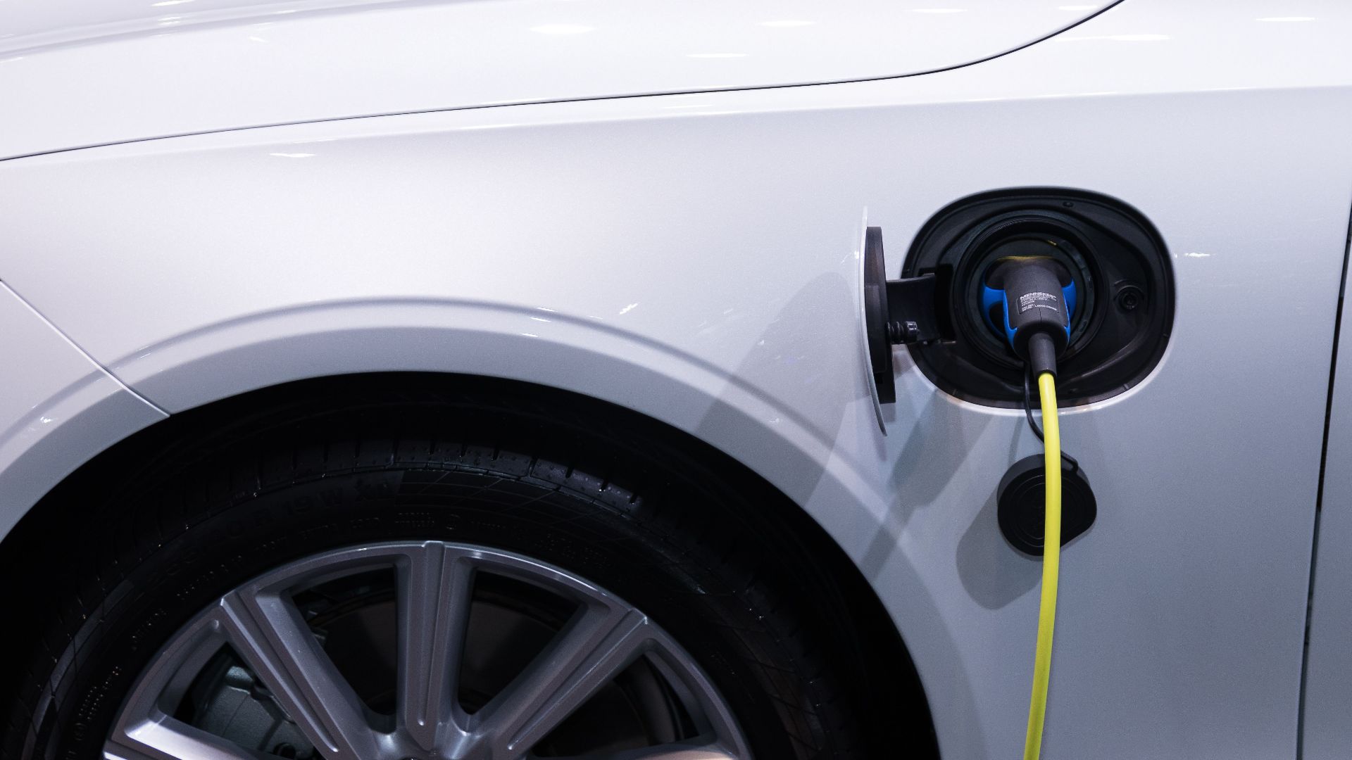 A white electric car is plugged in for charging, close-up view of the charging port.