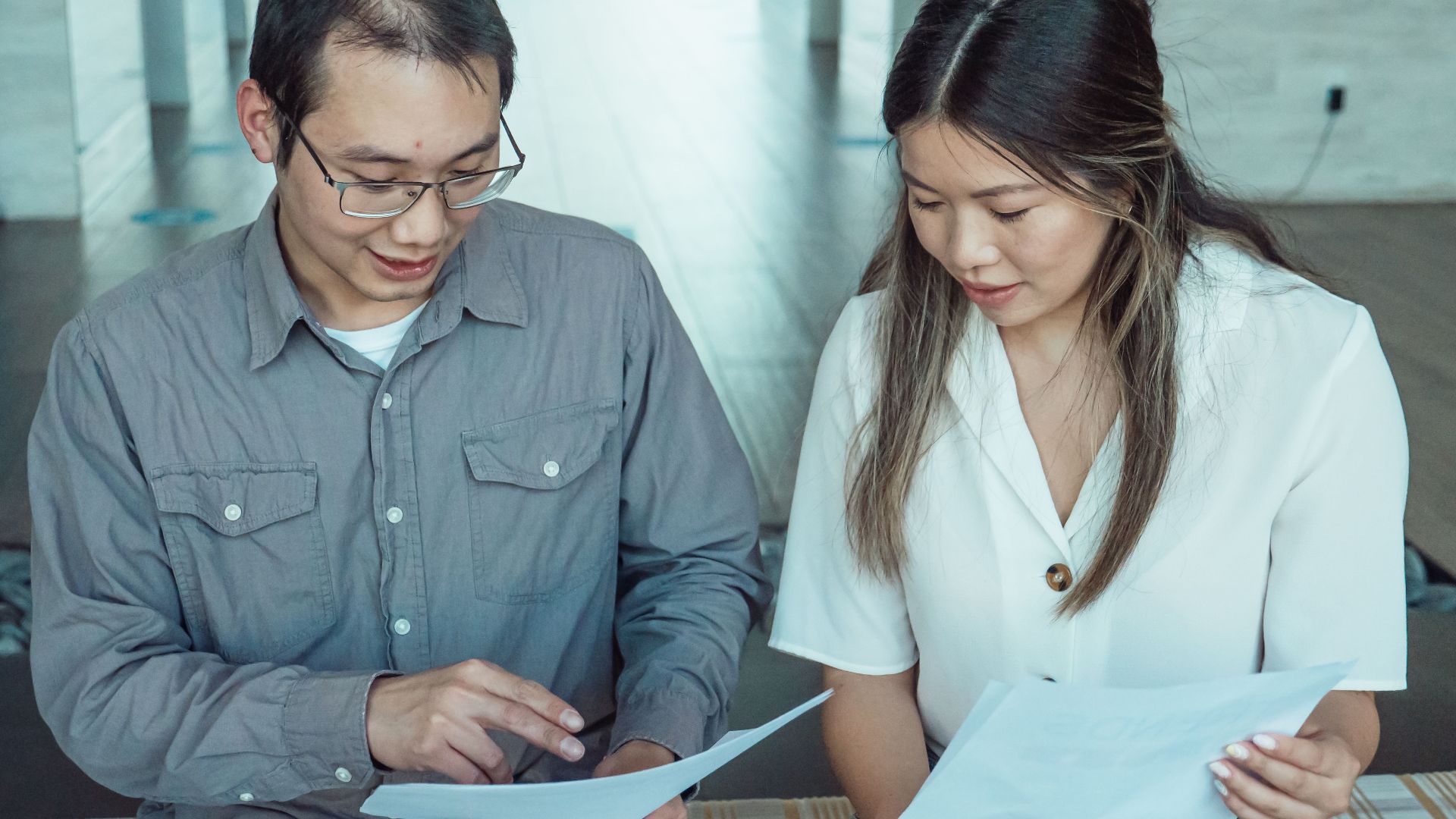 Two coworkers reviewing documents in a modern office, focused on teamwork and planning.