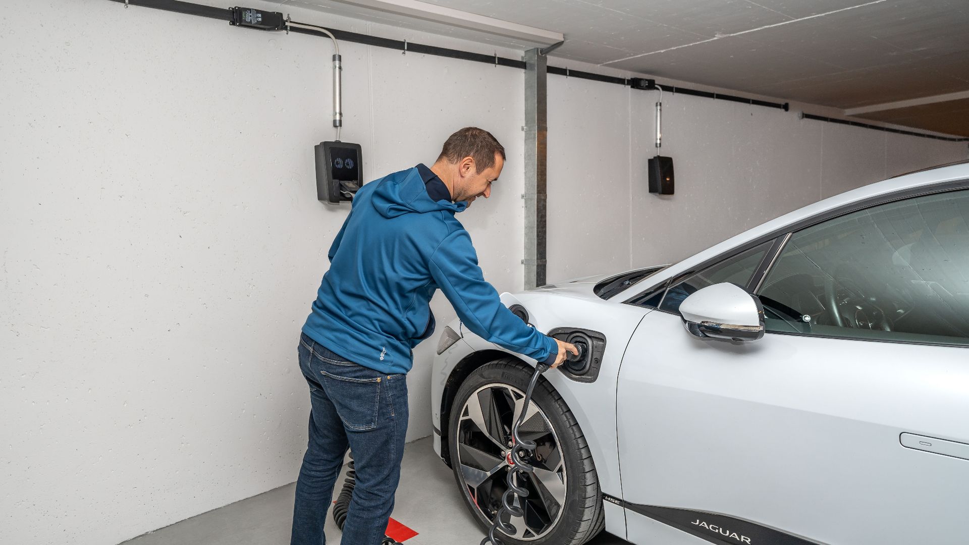 A man connects an electric car to a charging station in a modern indoor garage setting.