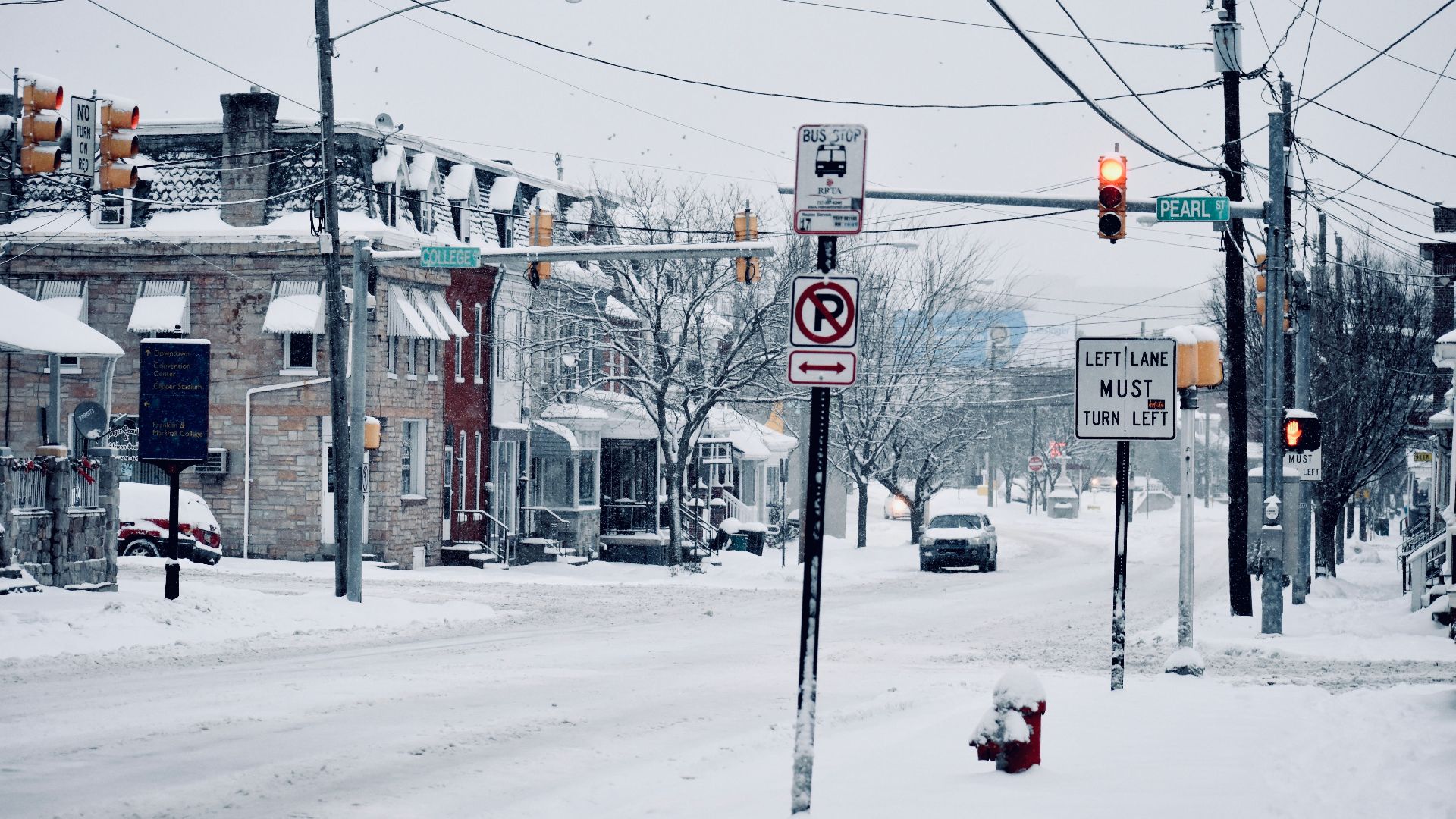 A winter street view in Lancaster, PA showcasing snowy roads, traffic signs, and parked vehicles.