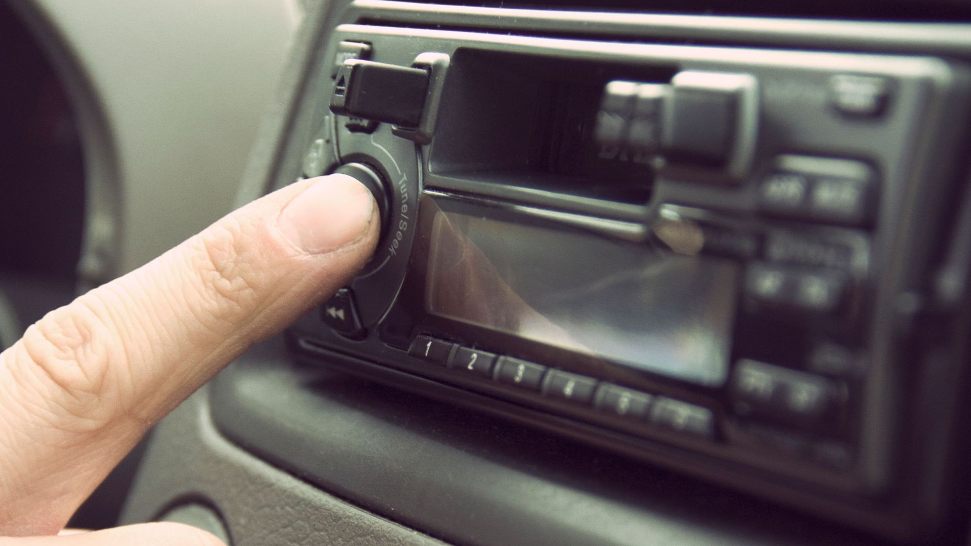 Finger adjusting car stereo in a vehicle's dashboard, depicting modern technology and music.