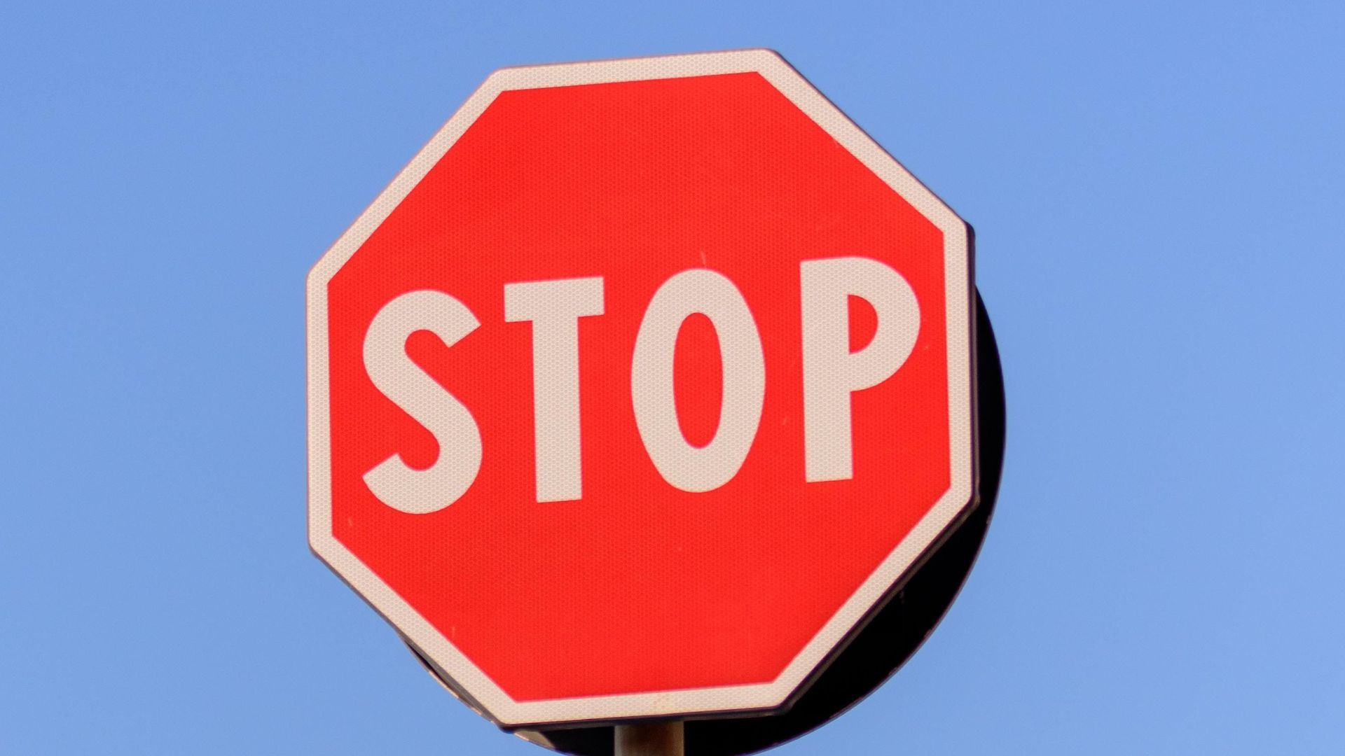 A red stop sign and blue forward arrow against a clear blue sky.