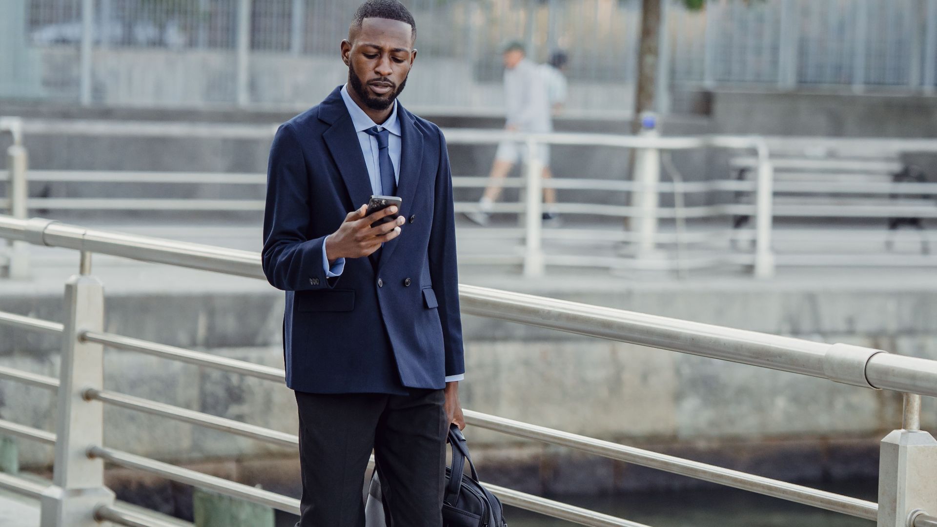 African American businessman walking on a city bridge, checking phone outdoors.