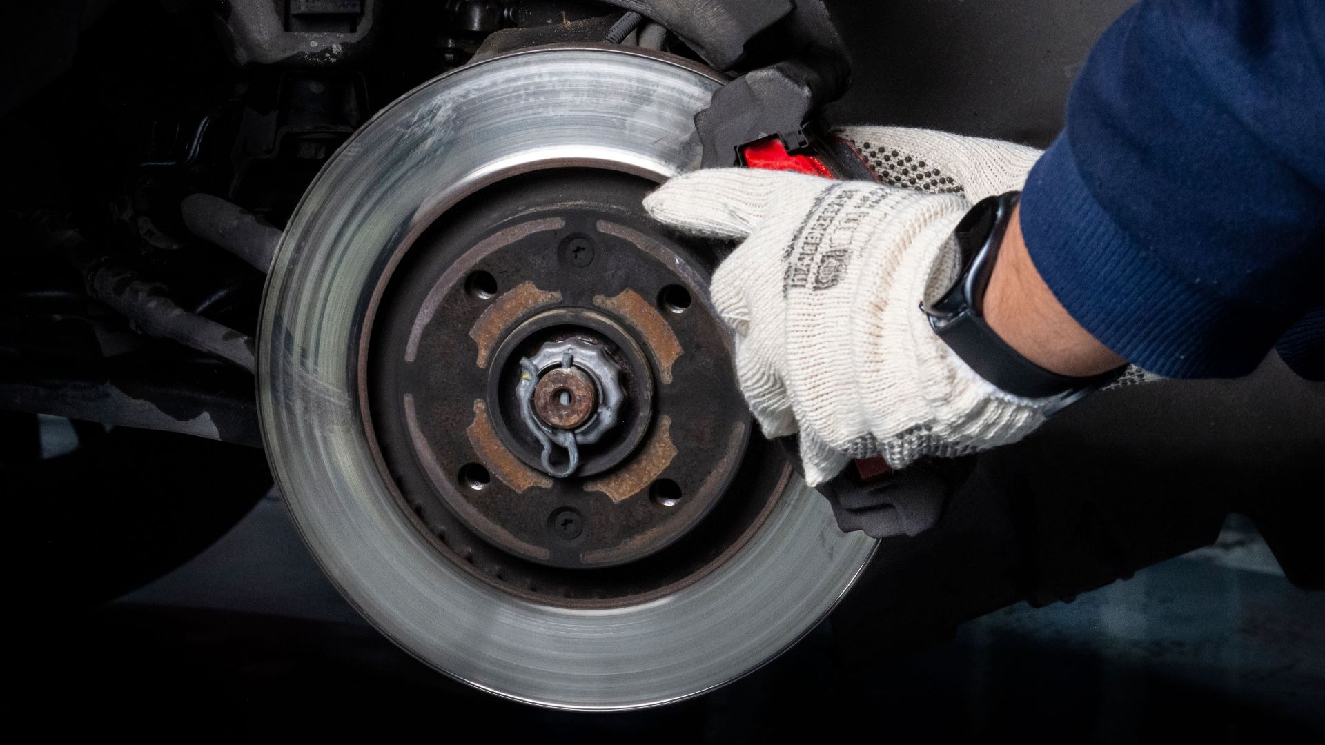 Mechanic working on car brake system in a workshop setting.