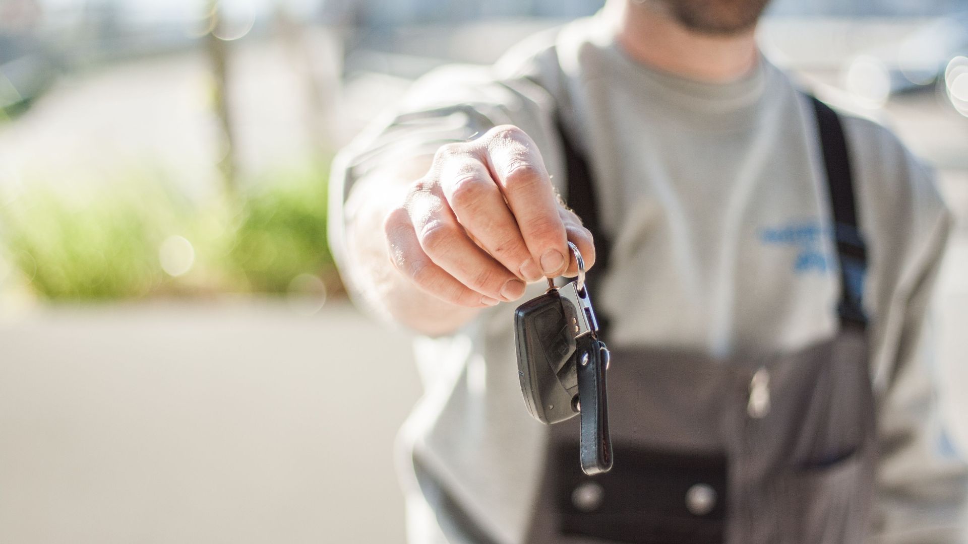 Hand holding a car key outdoors, blurred background, shallow focus.