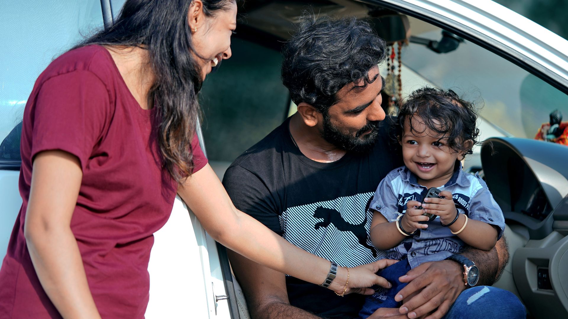 A joyful family moment with parents and child sitting in a car in Sanand, India.