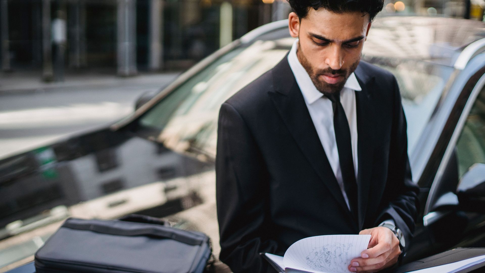 Confident businessman reviewing documents on the street beside a car.