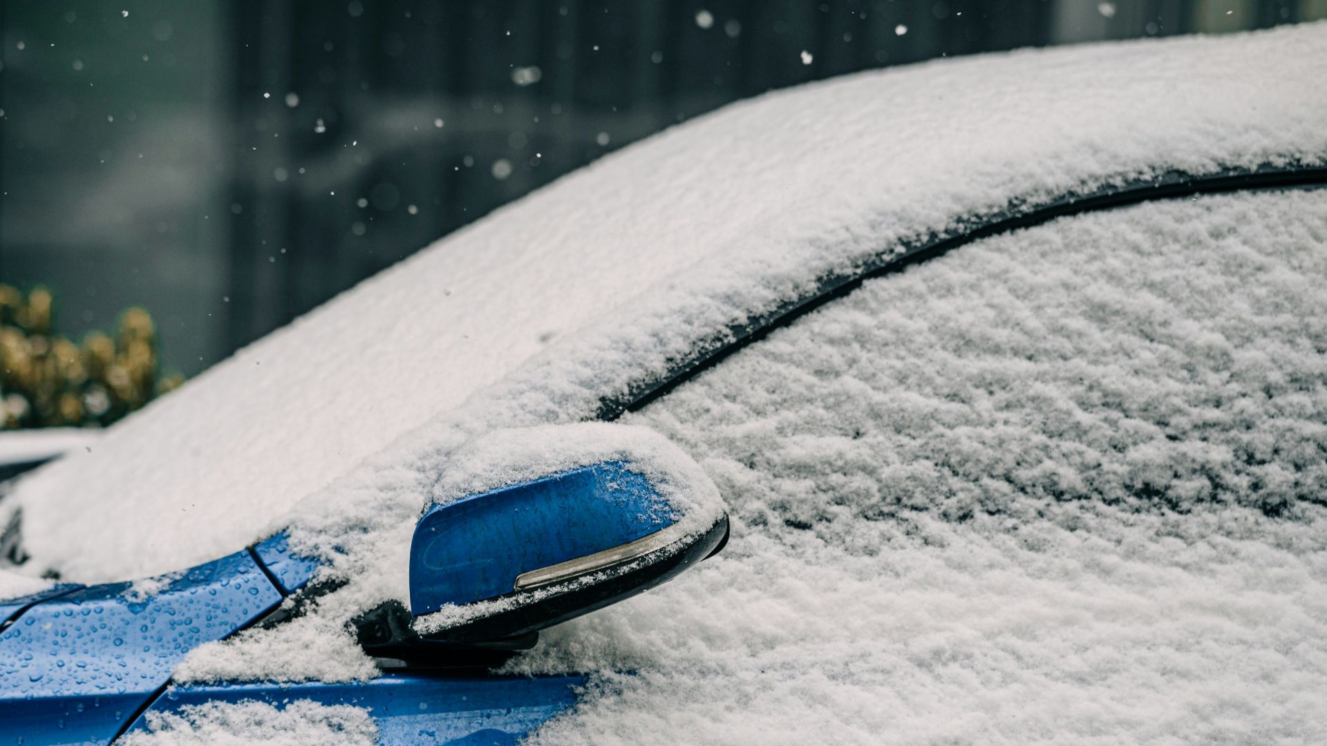 a blue car covered in snow in front of a building