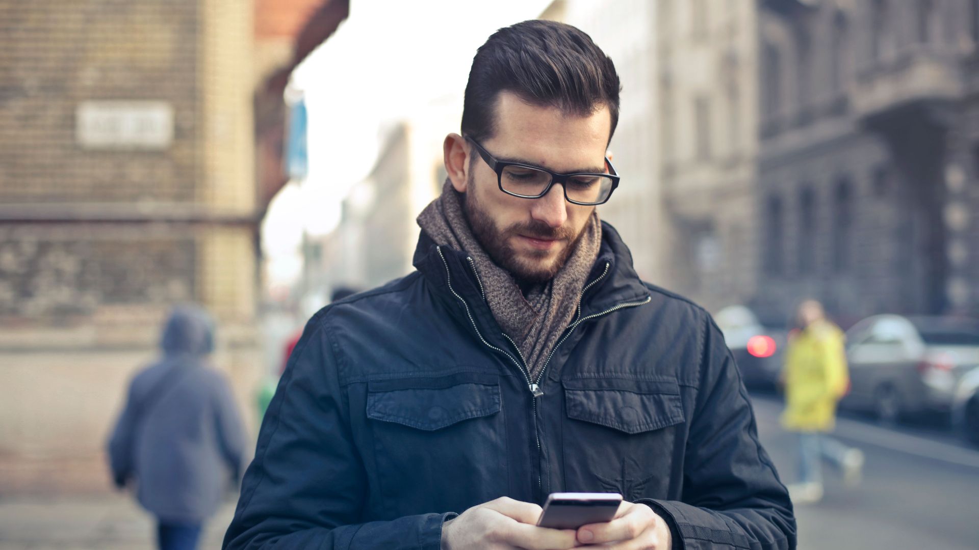 Adult man with glasses using a smartphone on a city street in Budapest, Hungary.