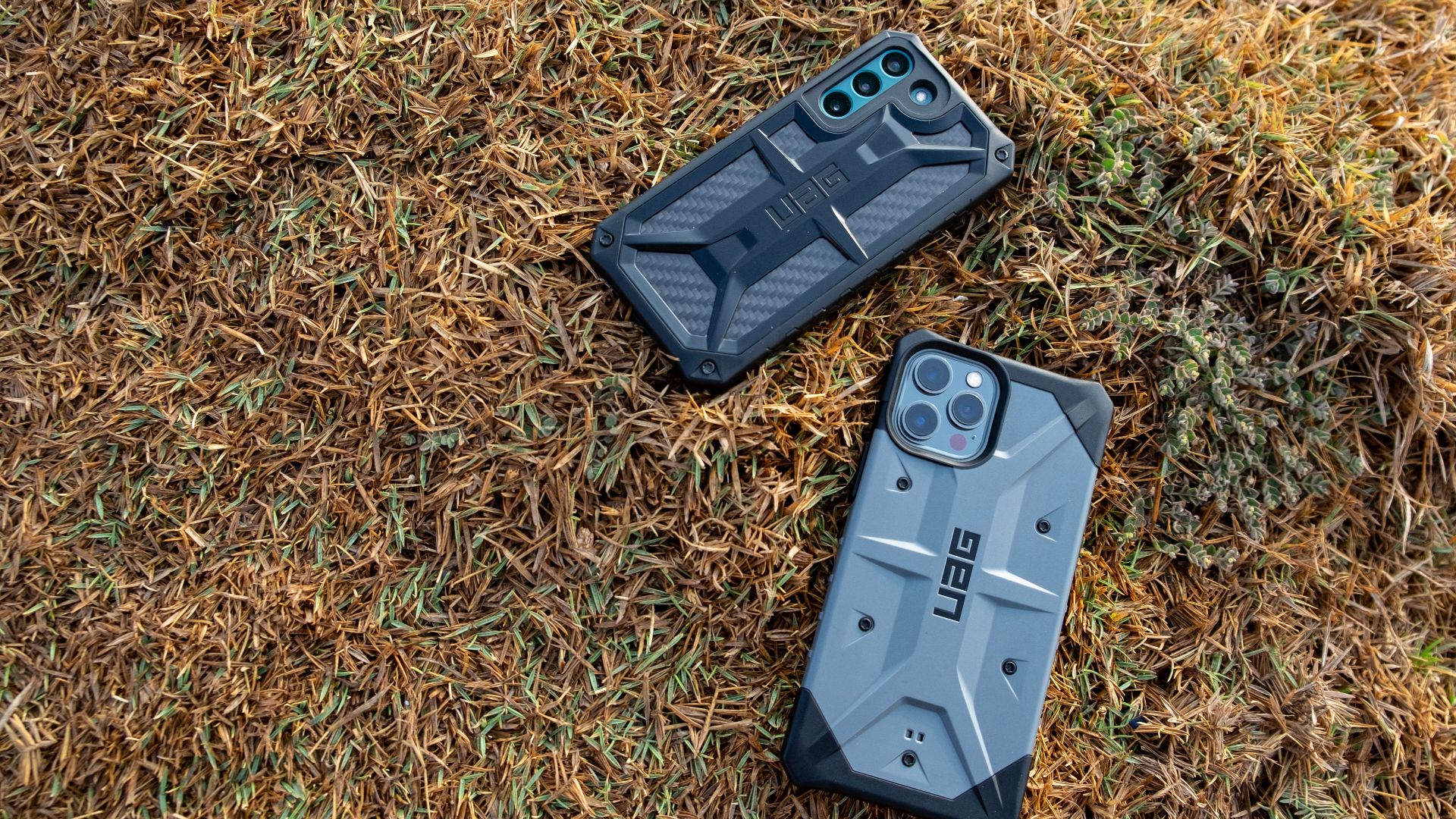 Rugged smartphone cases on grass, showcasing protective designs by UAG. Ideal for outdoor adventures.