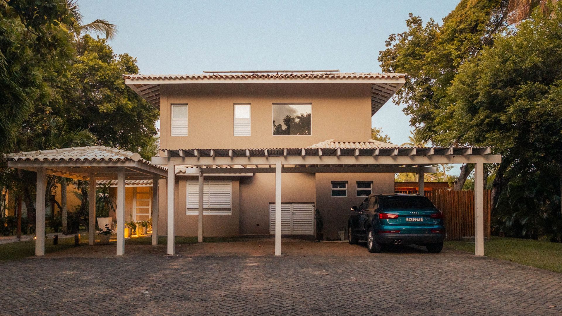 Exterior view of a modern house with a driveway and palm trees at sunset, offering a serene tropical ambiance.