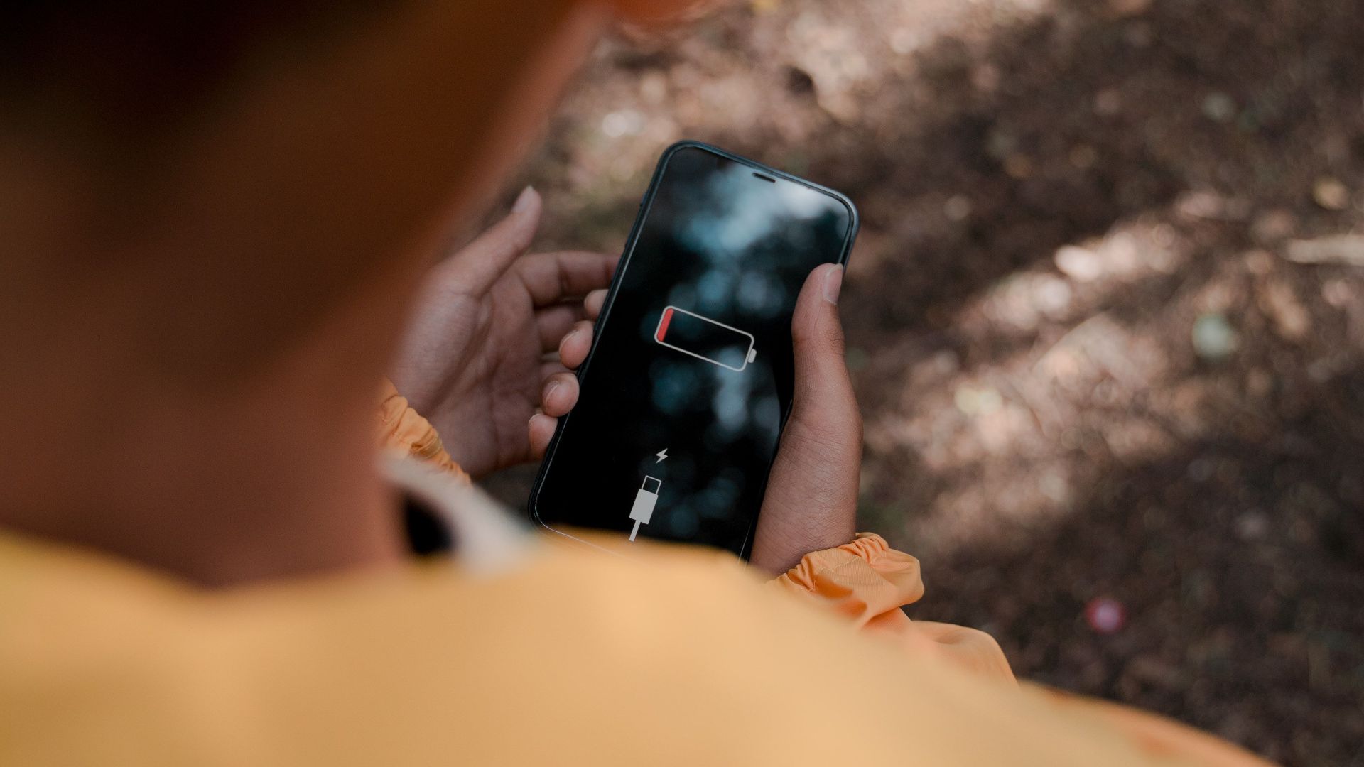 Teenager with low battery smartphone in forest reflects solitude and disconnect.