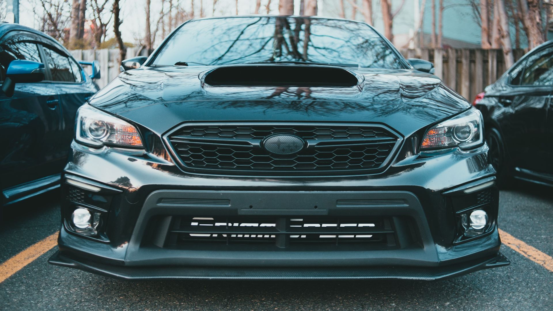 A sleek black Subaru Impreza with a prominent hood scoop, captured in an outdoor setting.