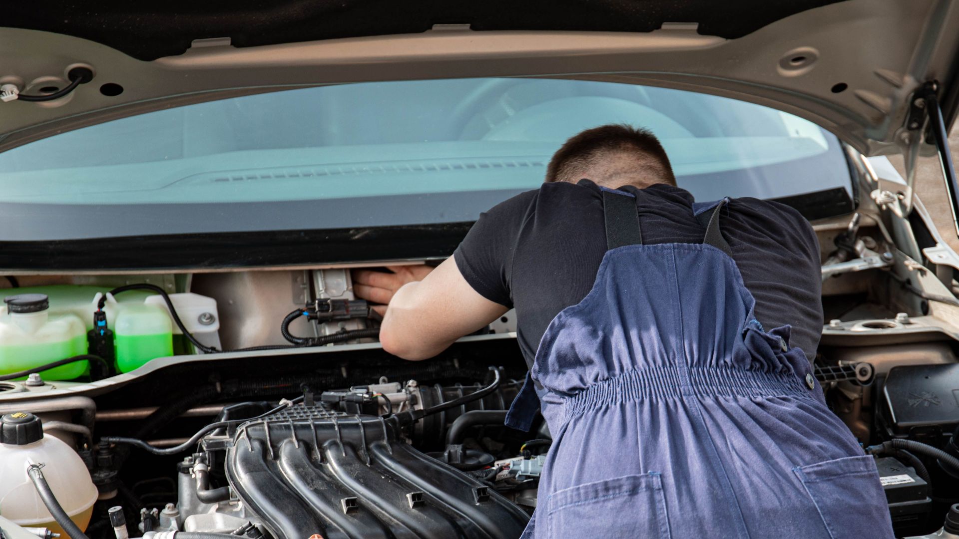 An automotive mechanic performing engine maintenance on a car outdoors, showcasing mechanical skills.
