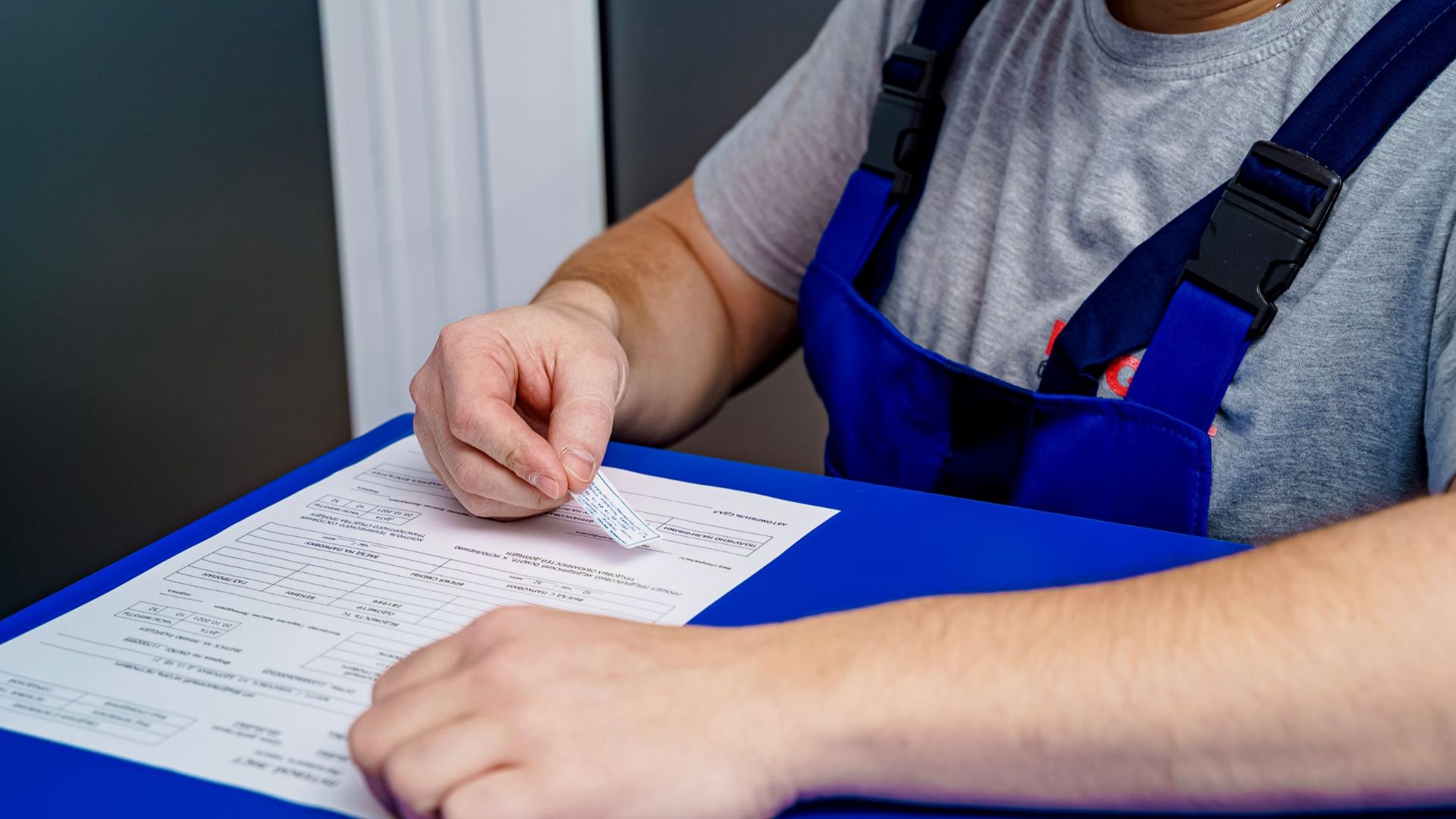 A mechanic in overalls reviews paperwork at a desk in an office setting.