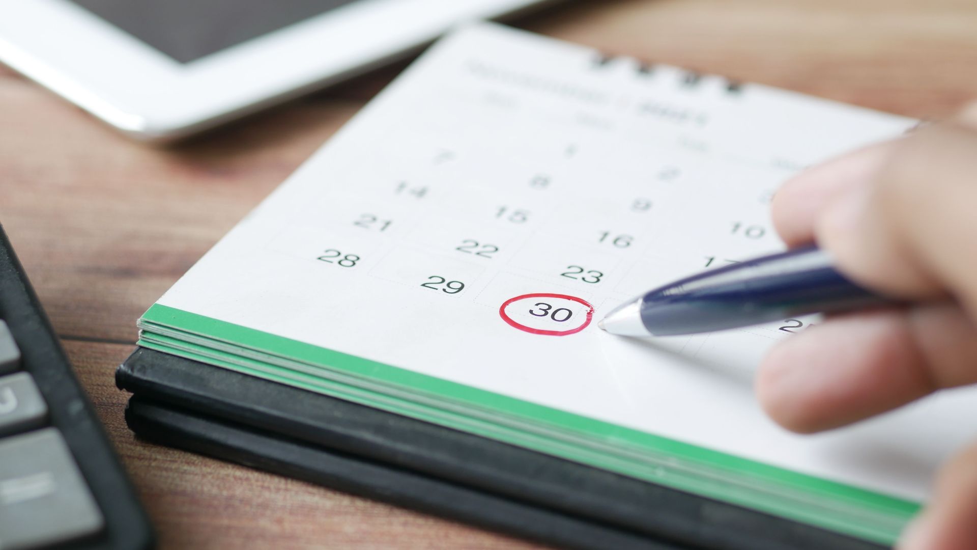 Close-up shot of a hand marking a date on a calendar with a pen, emphasizing planning and scheduling.