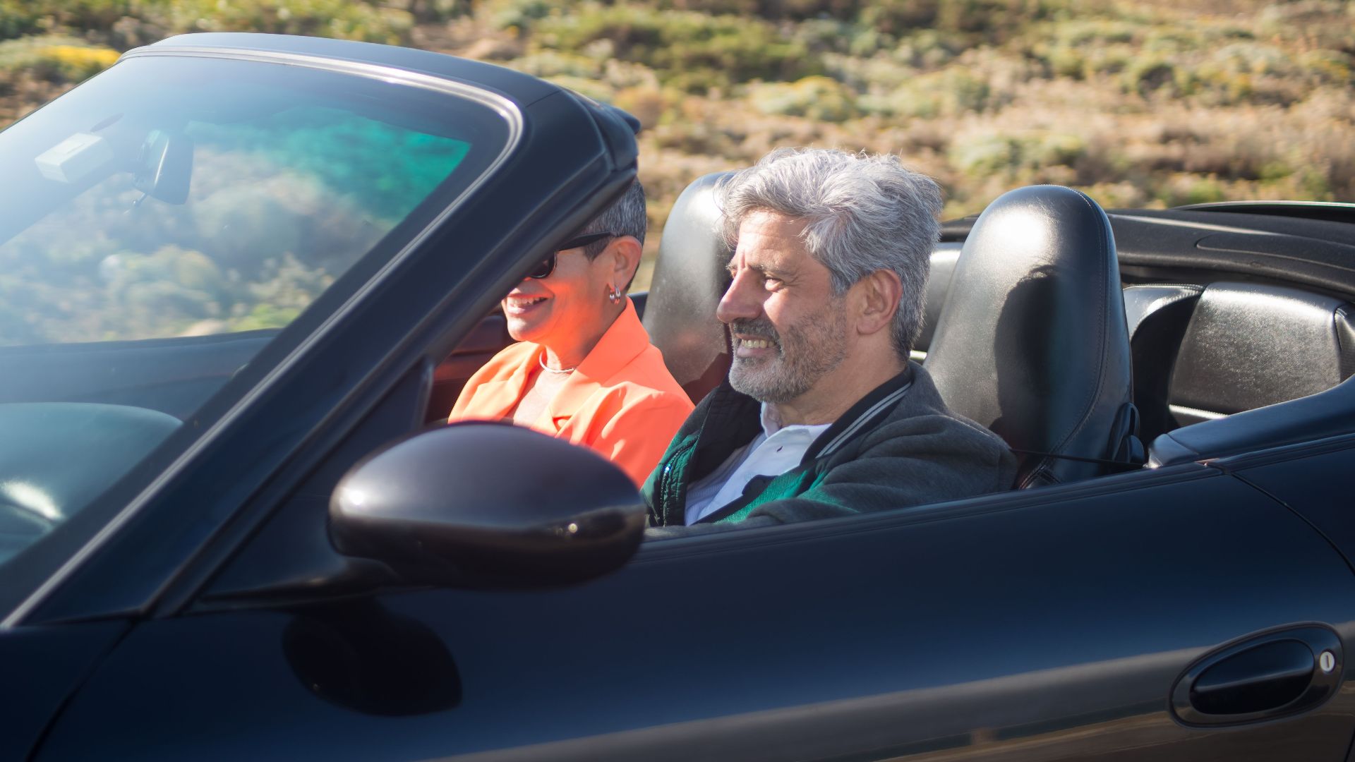 Happy senior couple driving a luxury convertible car on a sunny day outdoors in Portugal.
