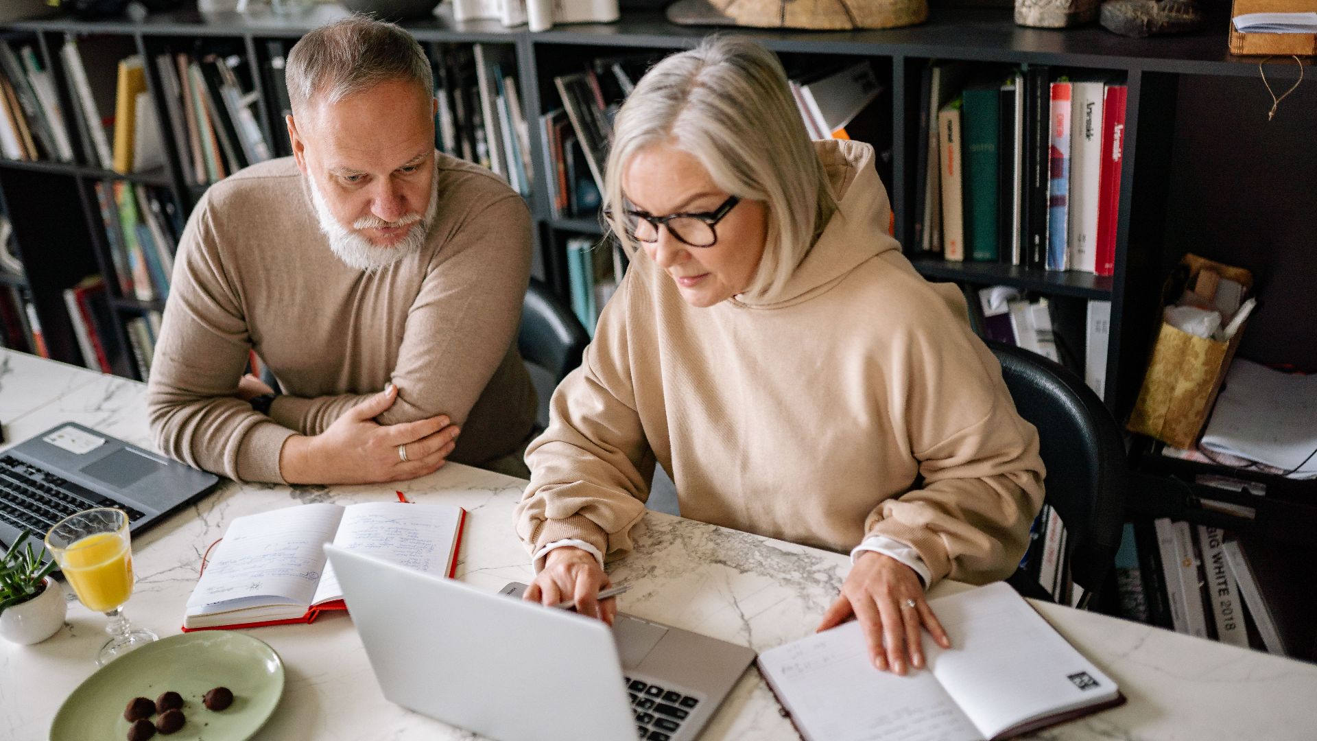 Elderly couple collaborating on laptops in a cozy home office setting.