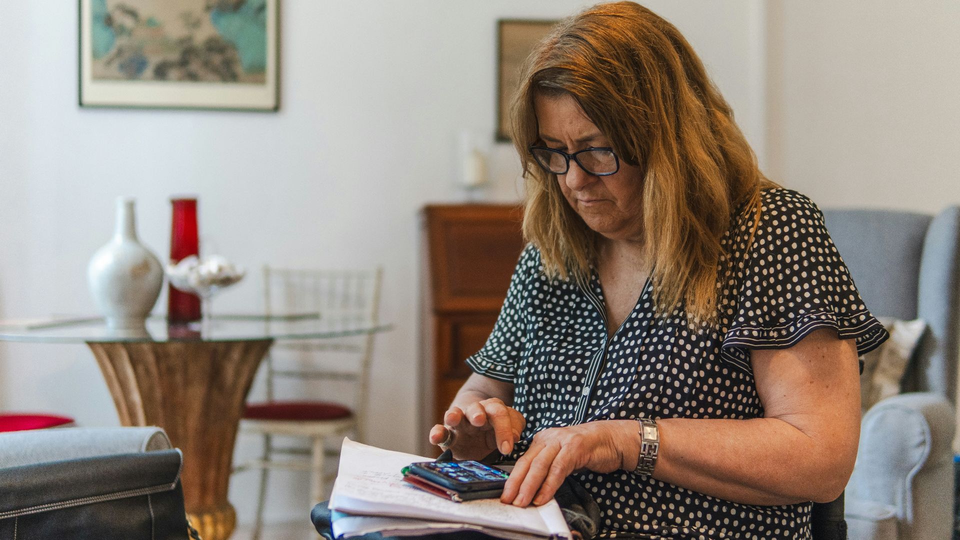 Woman using calculator with papers on table.