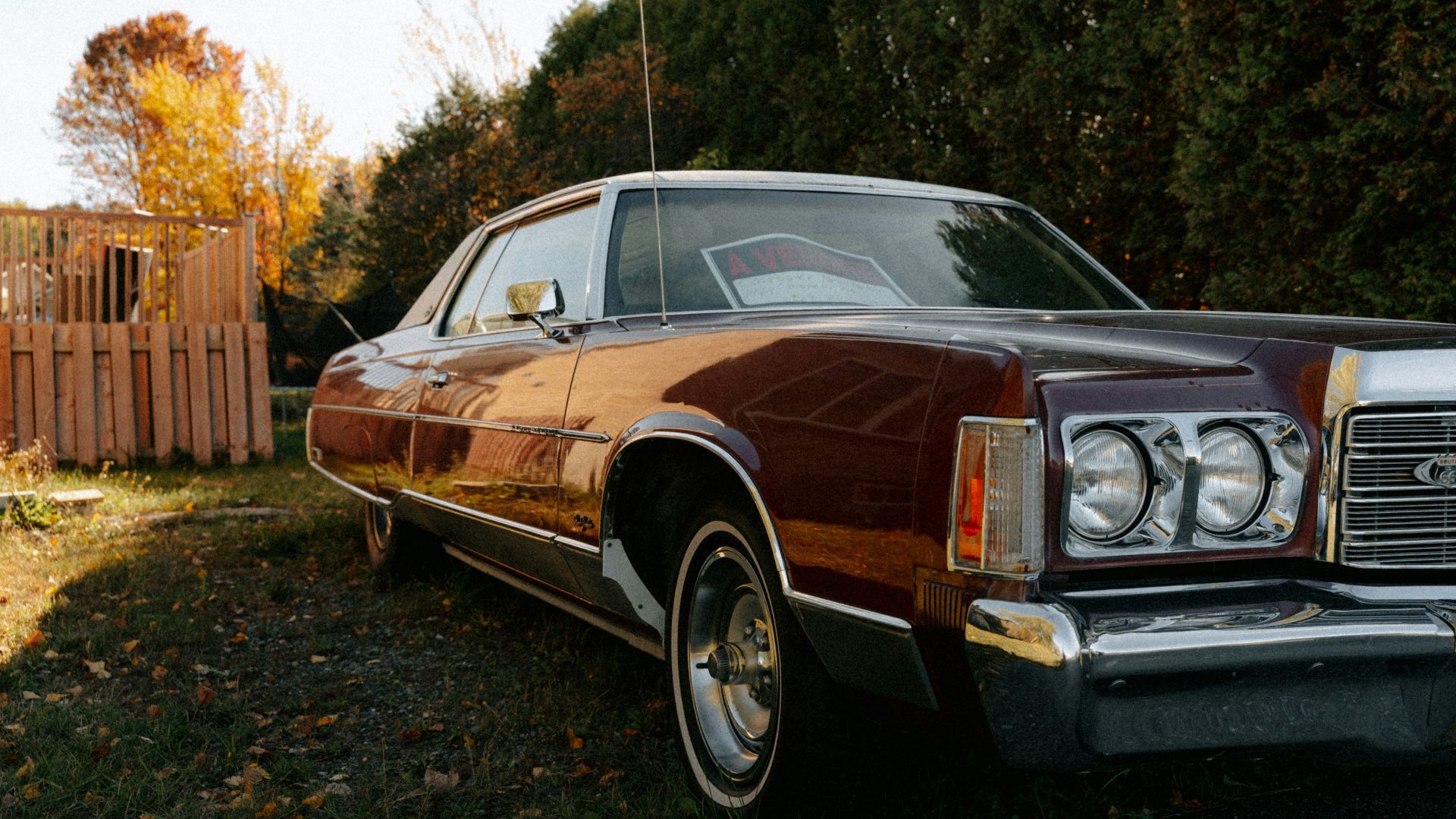 Vintage maroon car parked outdoors near trees.