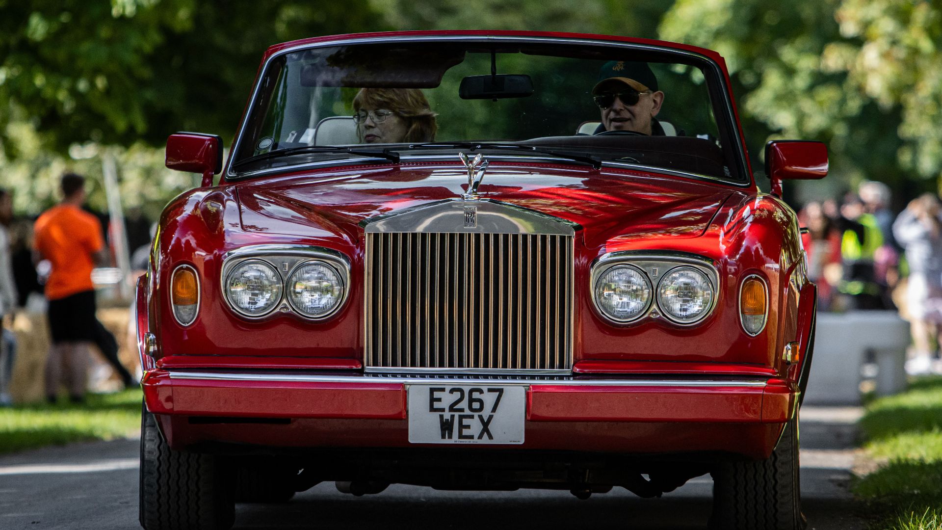 A classic red Rolls-Royce convertible driving down a city street with senior passengers.