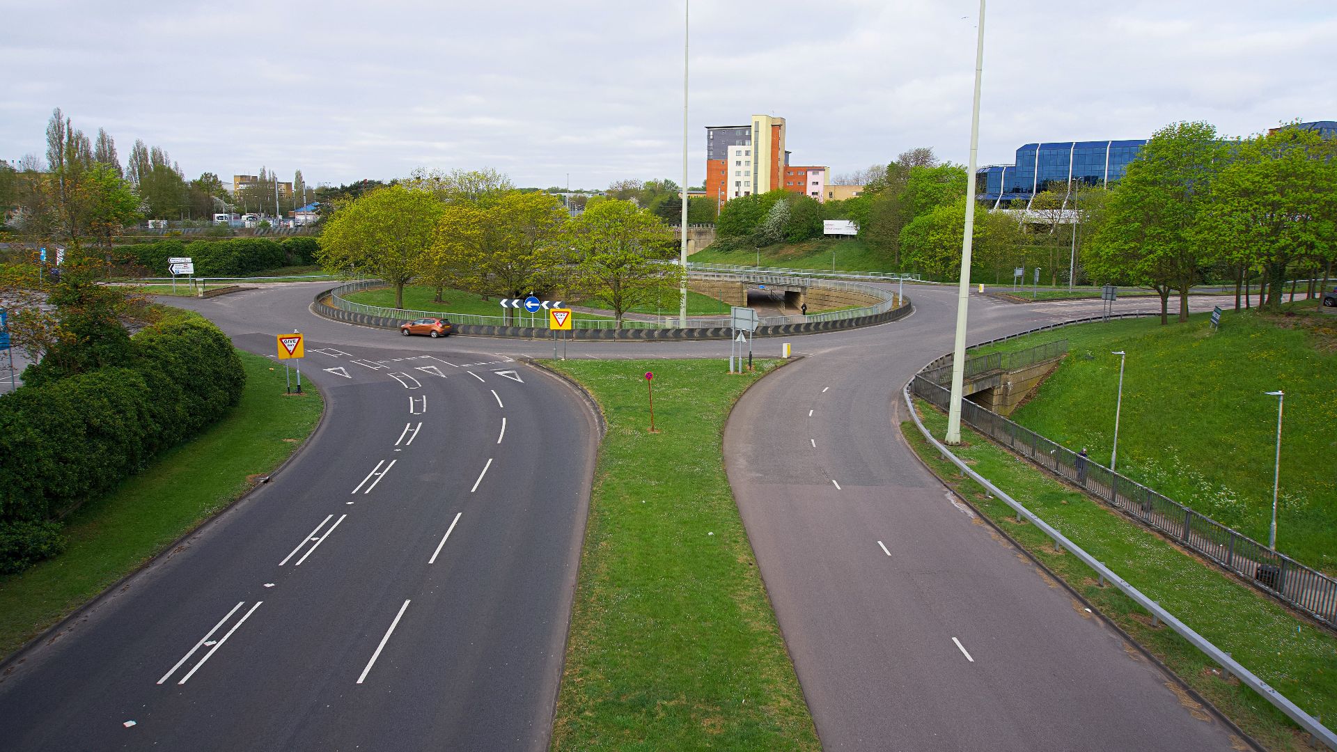 Roundabout with clear road markings surrounded by greenery and buildings in the background.