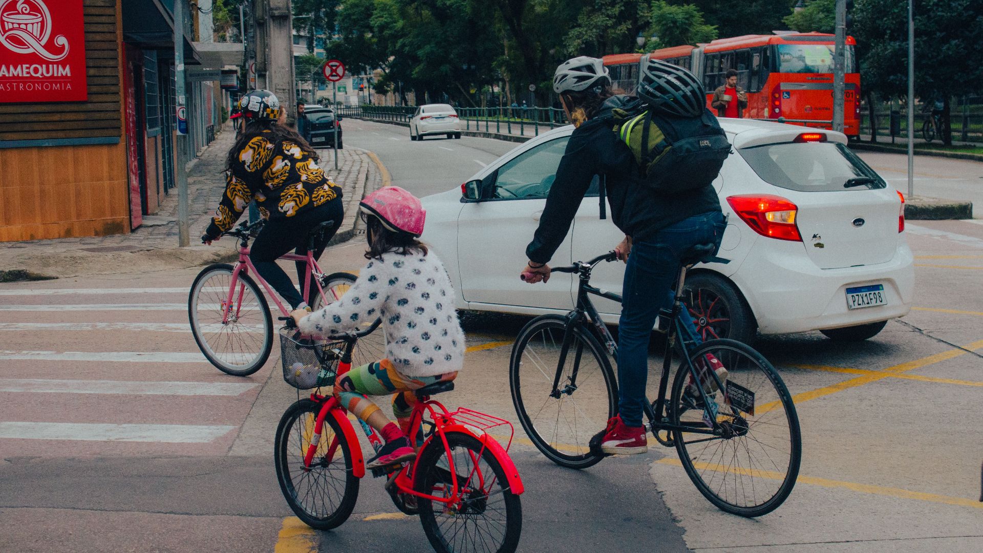 A family biking through a city intersection on a cloudy day, wearing helmets for safety.