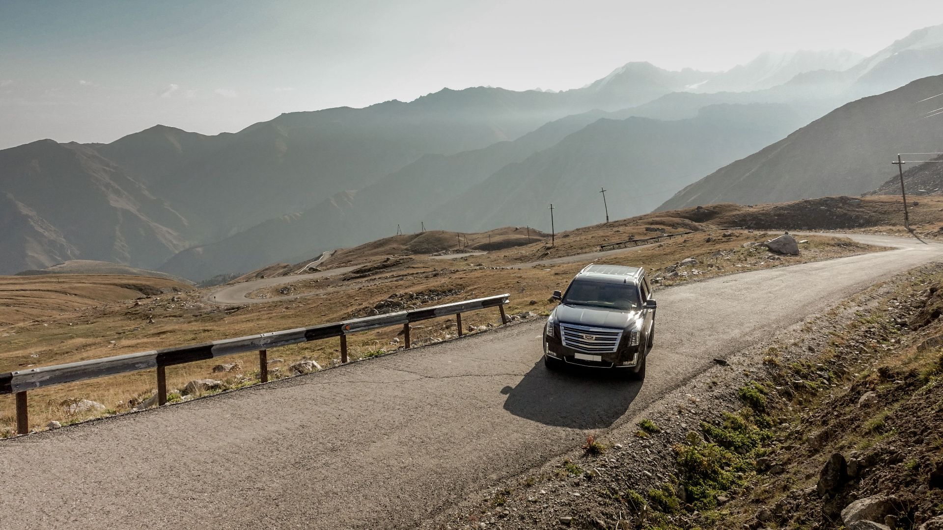 A scenic drive through Almaty's mountain ranges with a parked SUV during the day.