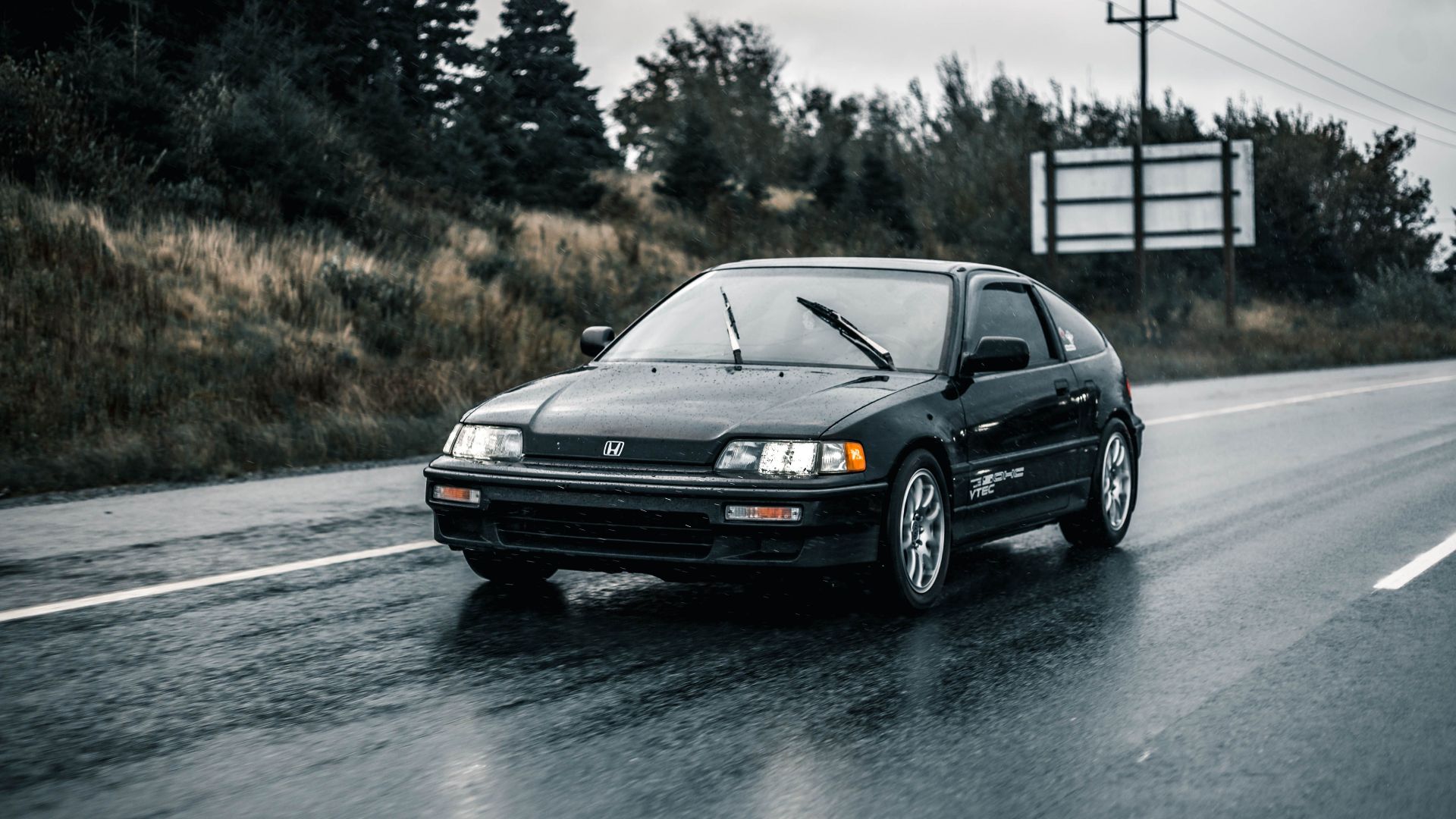 Black Honda car driving on wet road during rain, showcasing transportation in action.