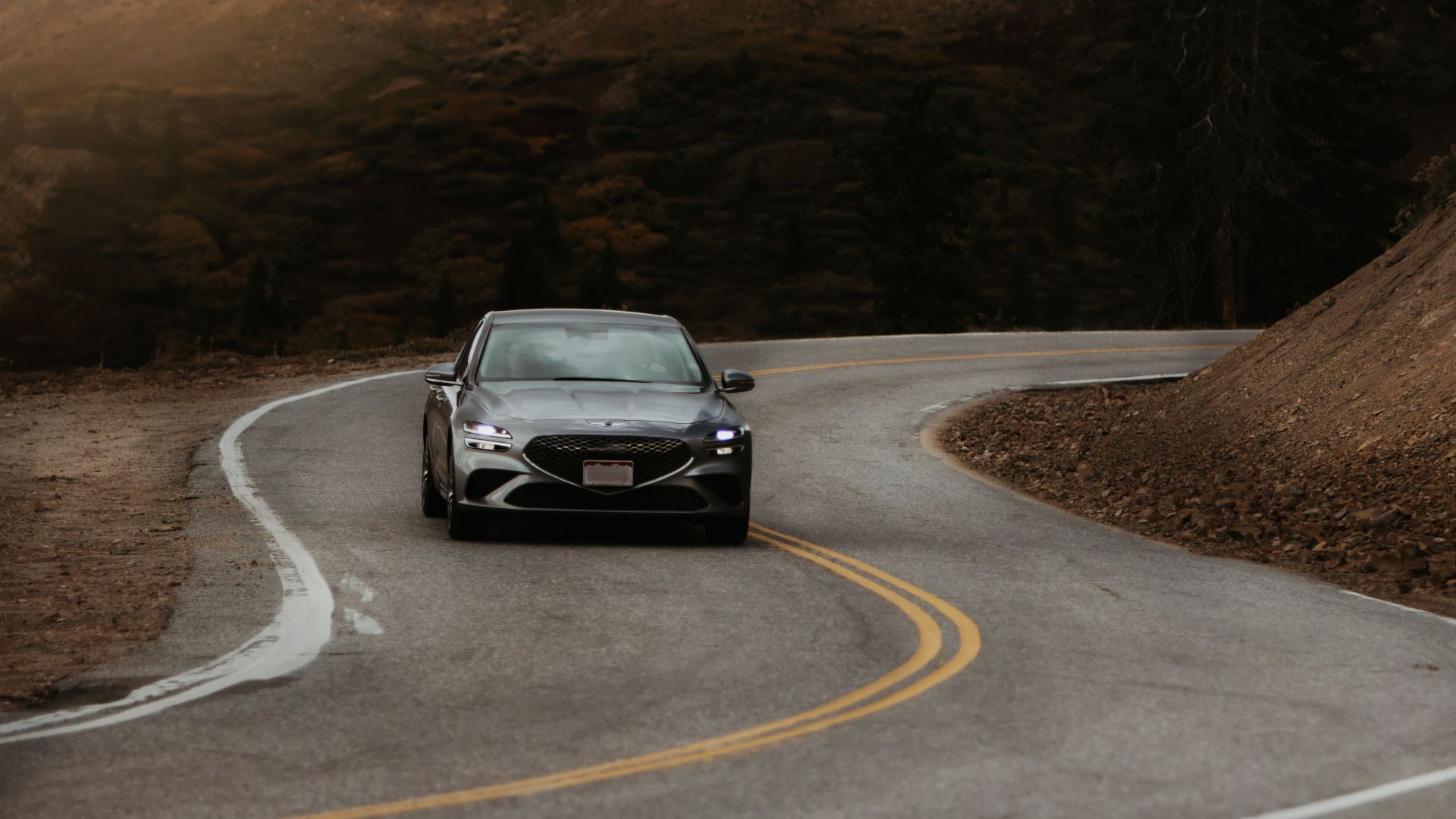 Car navigating a scenic winding road in Colorado with moody mountain backdrop.