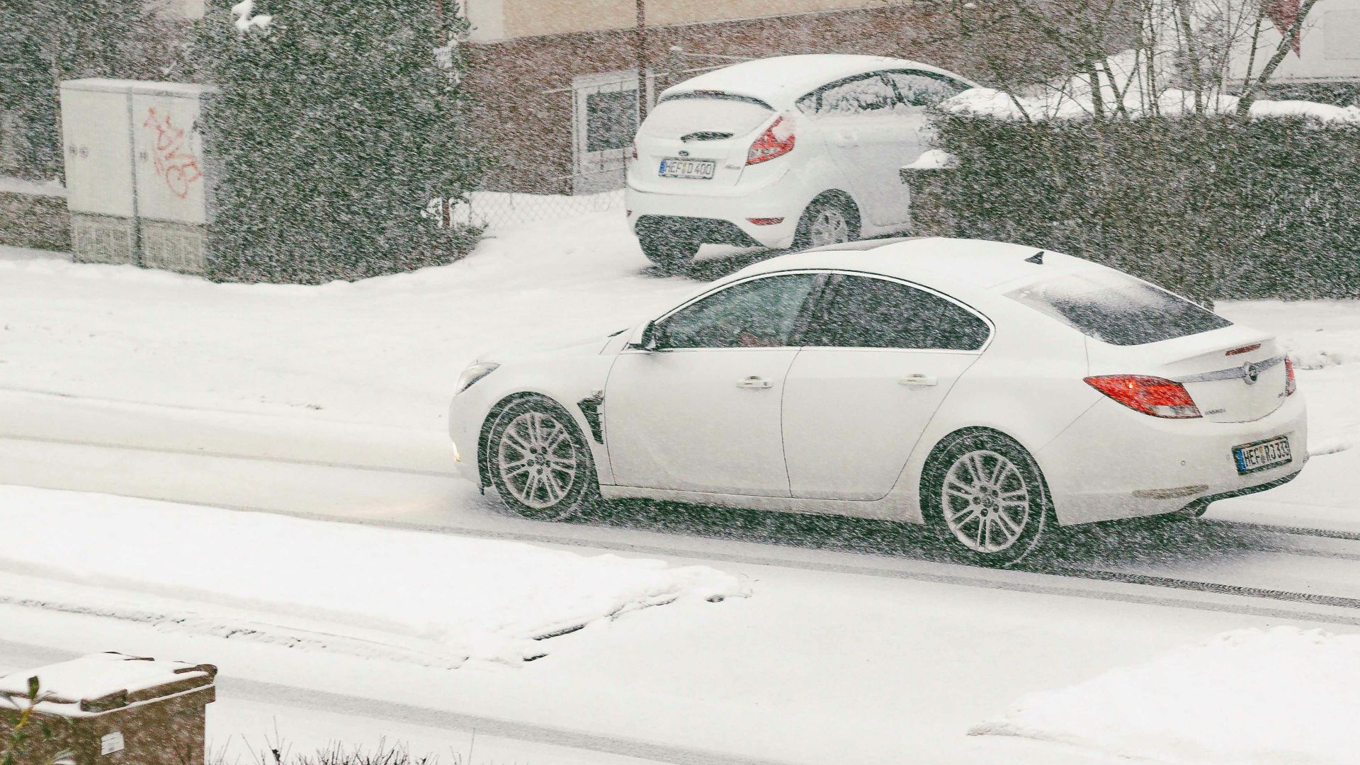 Two white cars driving on a snowy street.