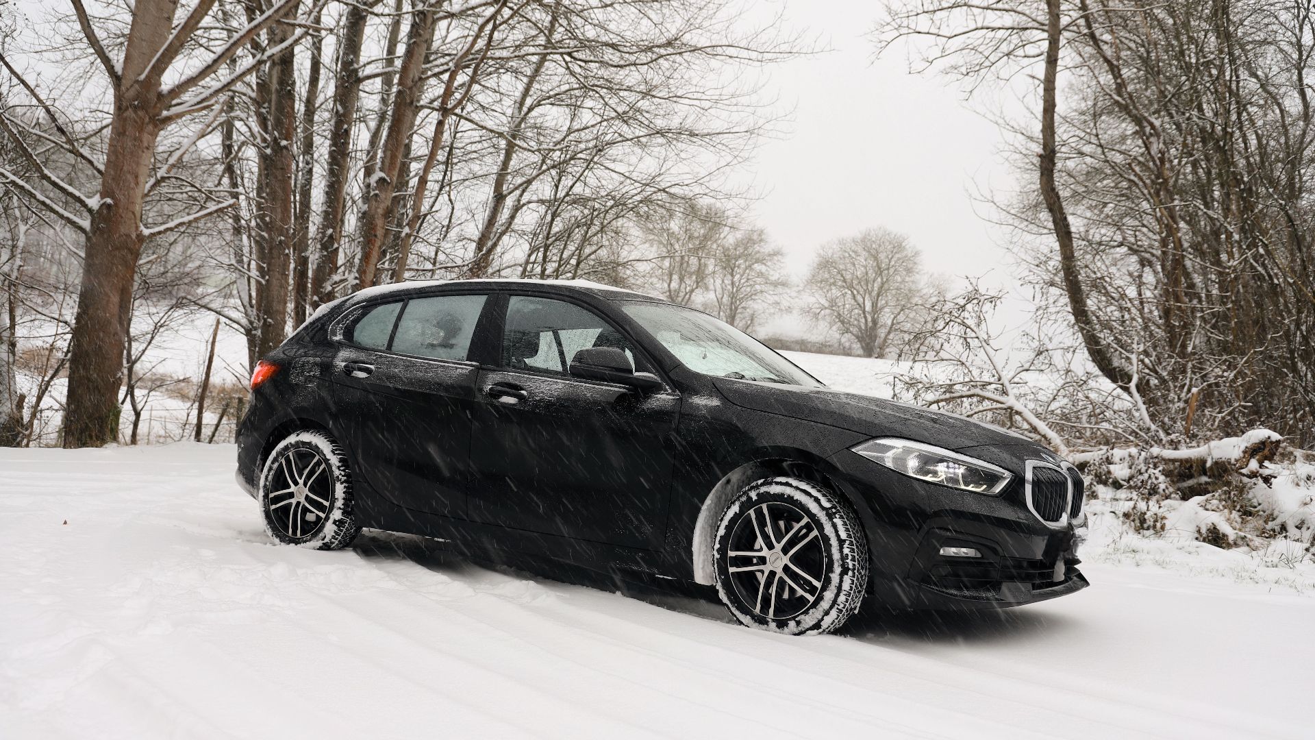 A black car driving through a snowy forest landscape, embodying winter weather's beauty.
