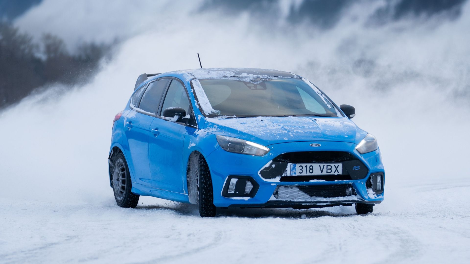 Blue car navigating snowy terrain in a mountainous winter setting.