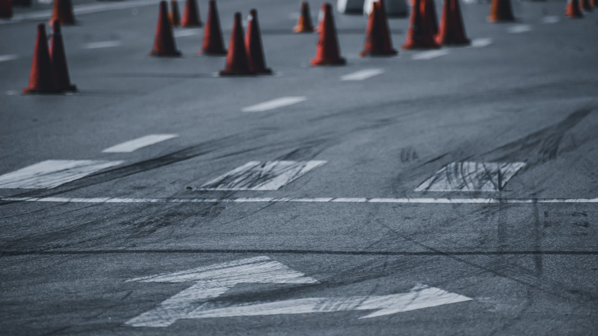 Asphalt roadway with black wheel tracks and red road cones placed on city street in daytime
