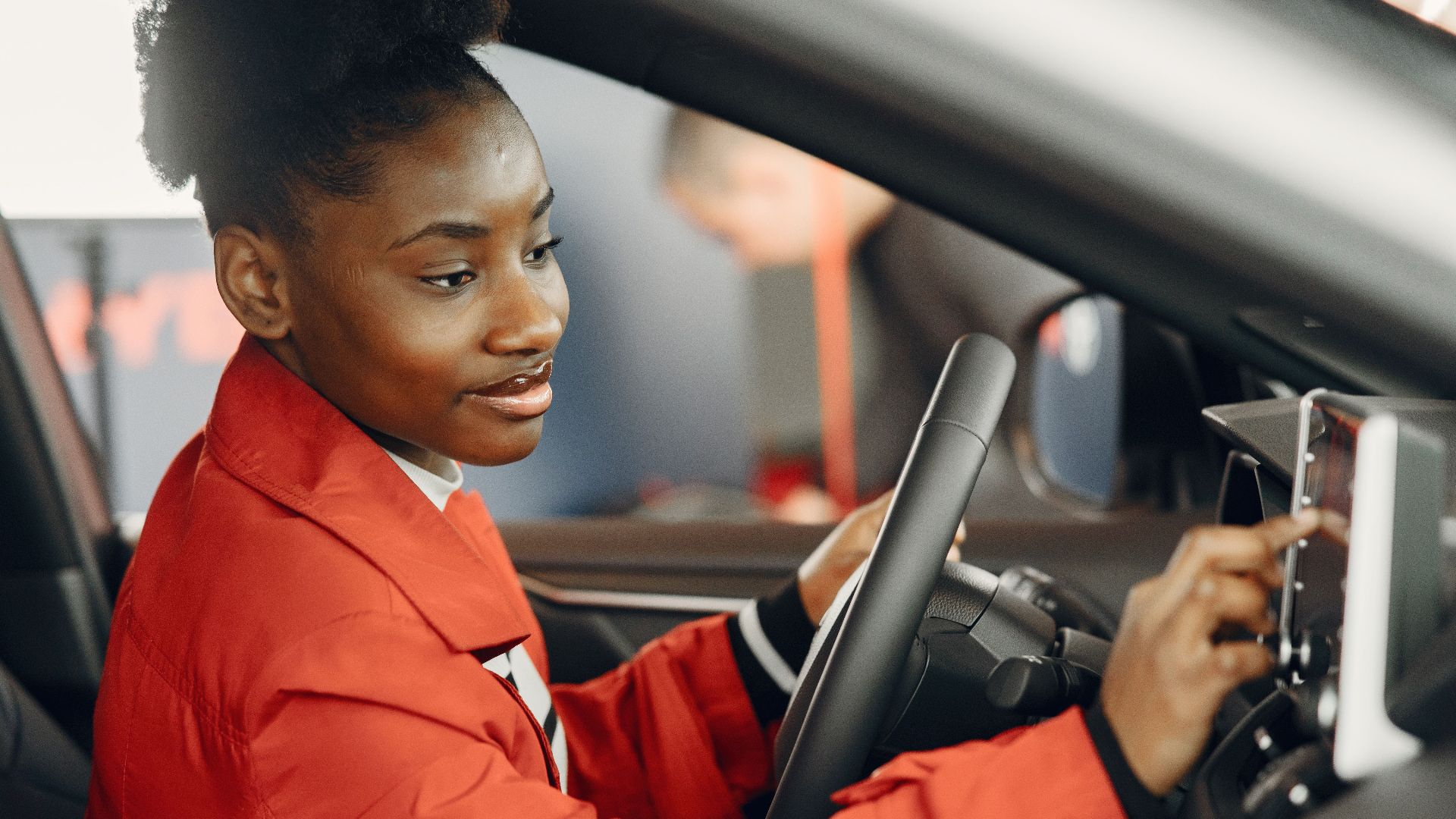 Young woman in red coat using touch screen in car interior.
