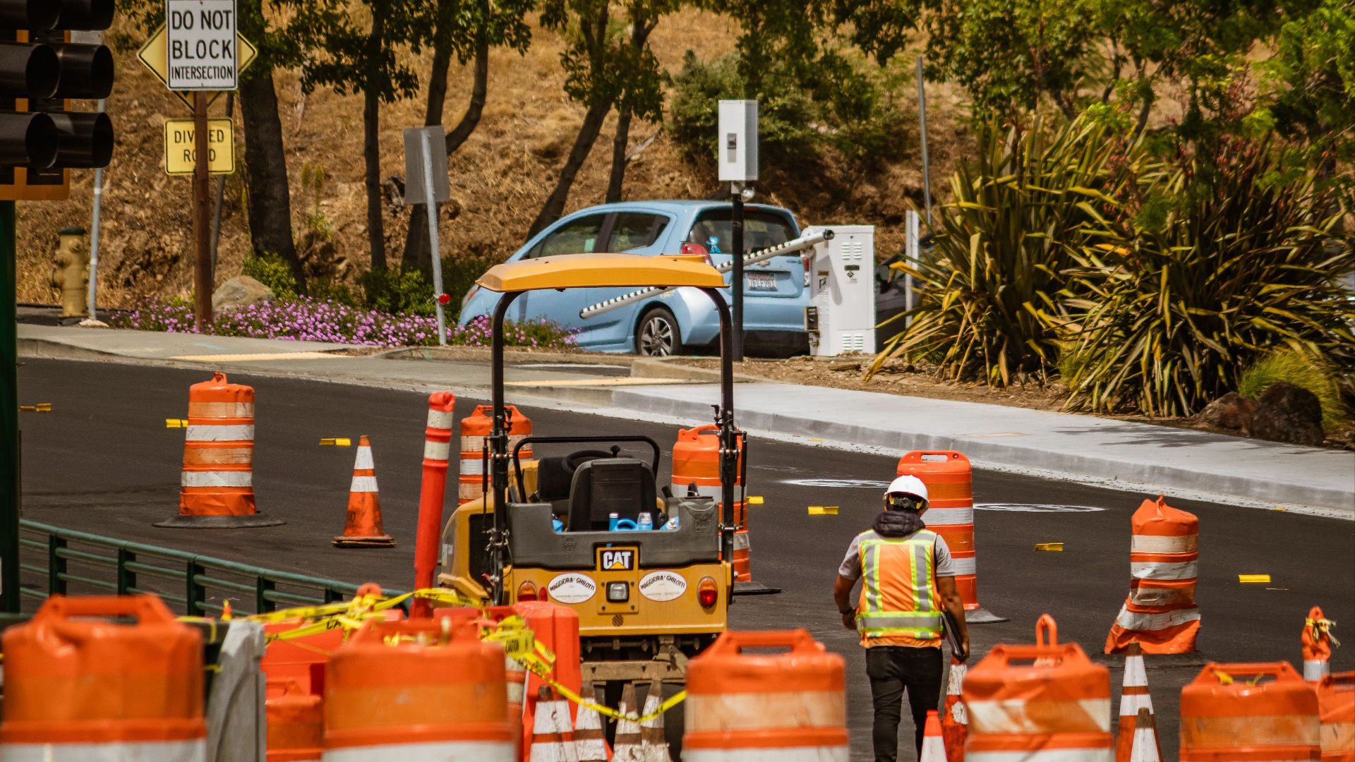A road construction worker surrounded by safety cones on a street in daylight.