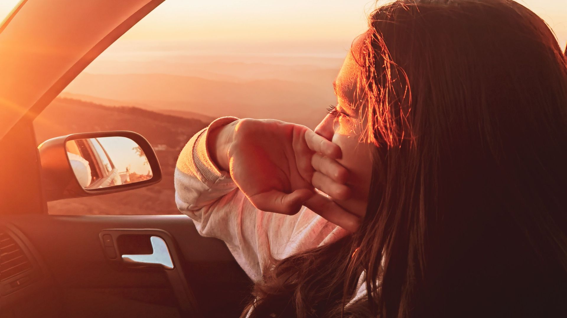 A woman relaxing and enjoying the sunset view from a car window, capturing a serene travel moment.