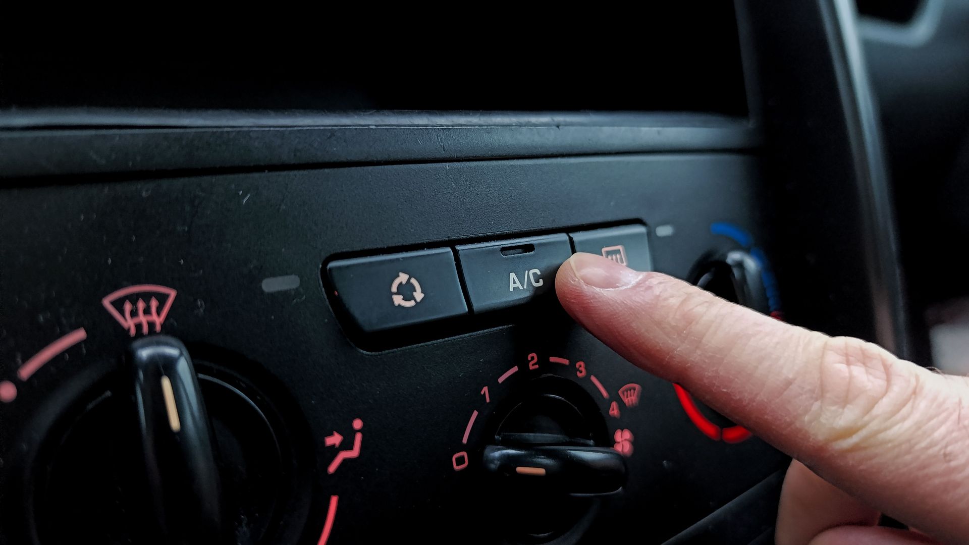 Close-up of a person adjusting a car's air conditioning system inside a vehicle cabin.