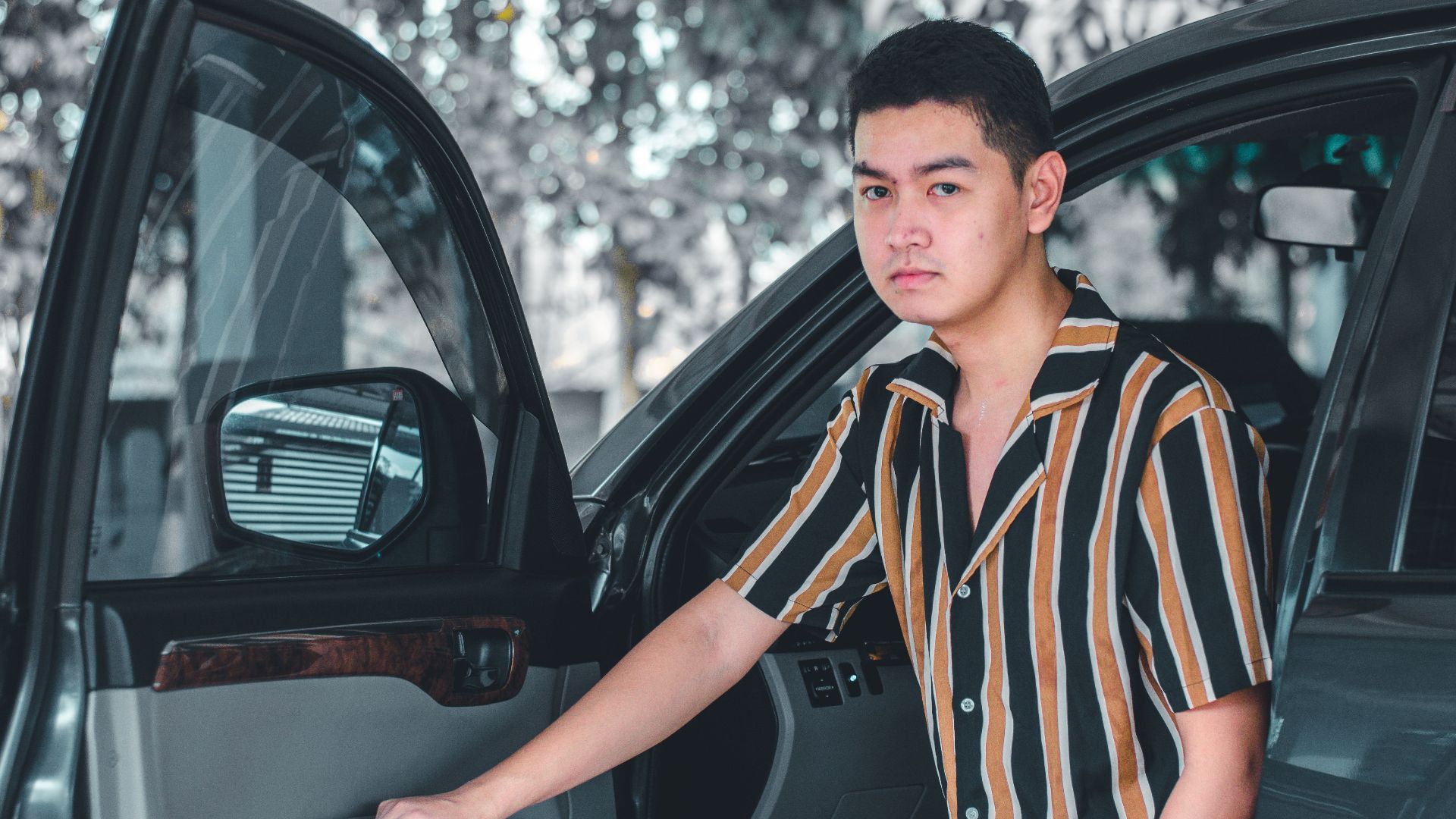 Portrait of a young man with a striped shirt standing beside an open car door.