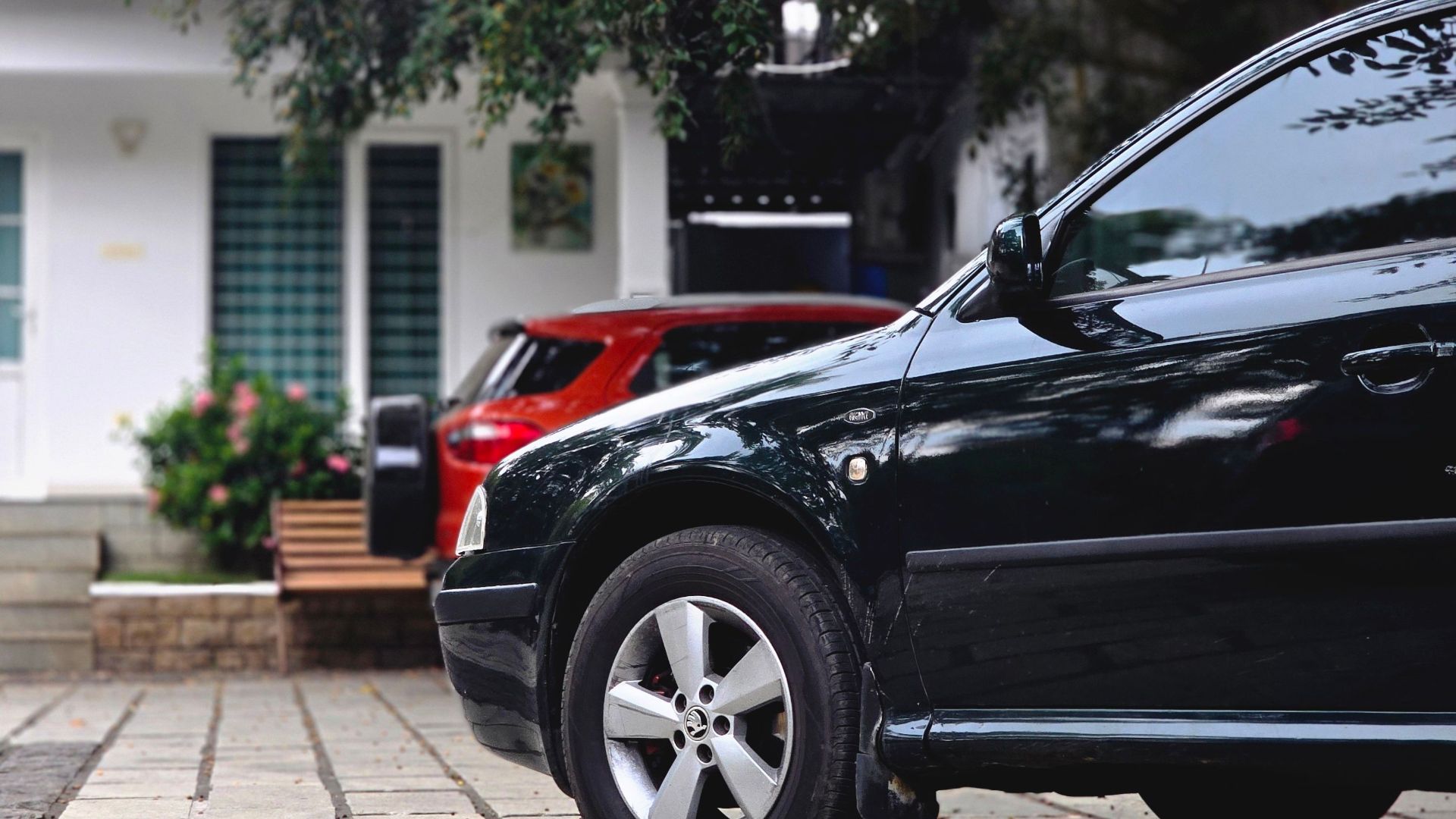 Close-up view of cars parked in a driveway with a modern house in the background.