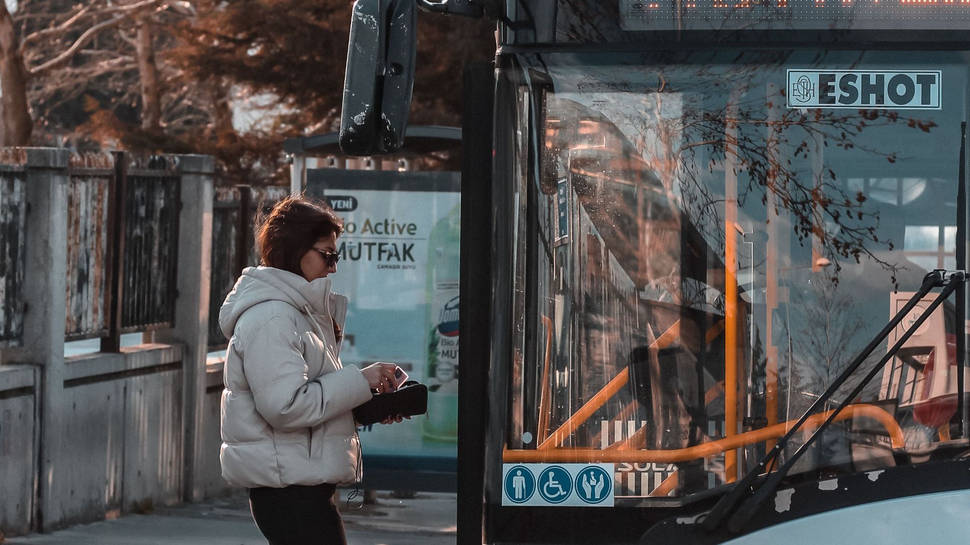 A woman in a jacket boards a public bus in Izmir, Turkey during the day.