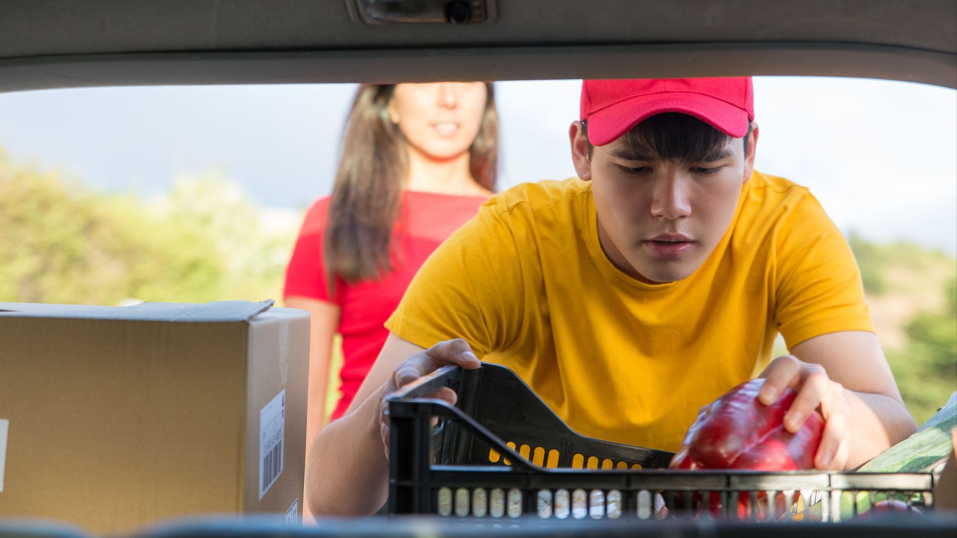 Man in yellow shirt loading groceries into a vehicle, outdoors.