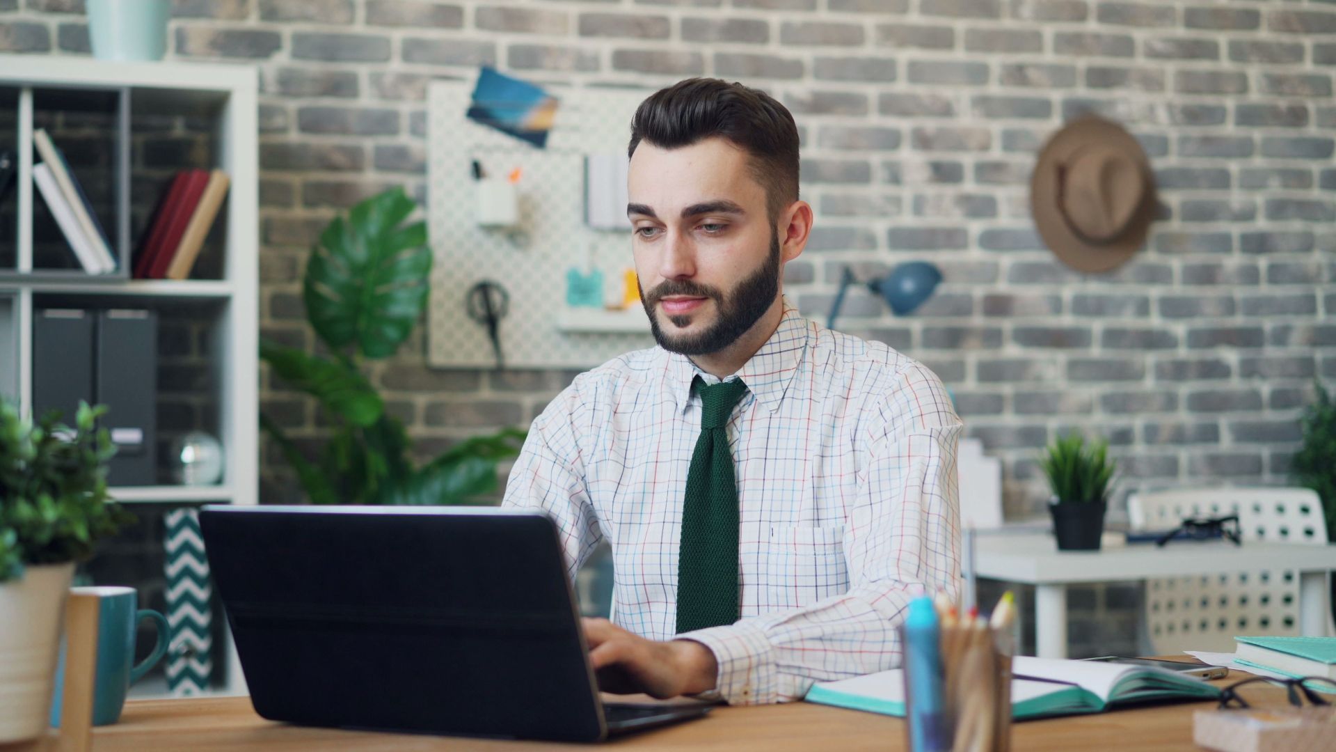 A young man in a modern office setting working on a laptop, showcasing a stylish and contemporary workspace.