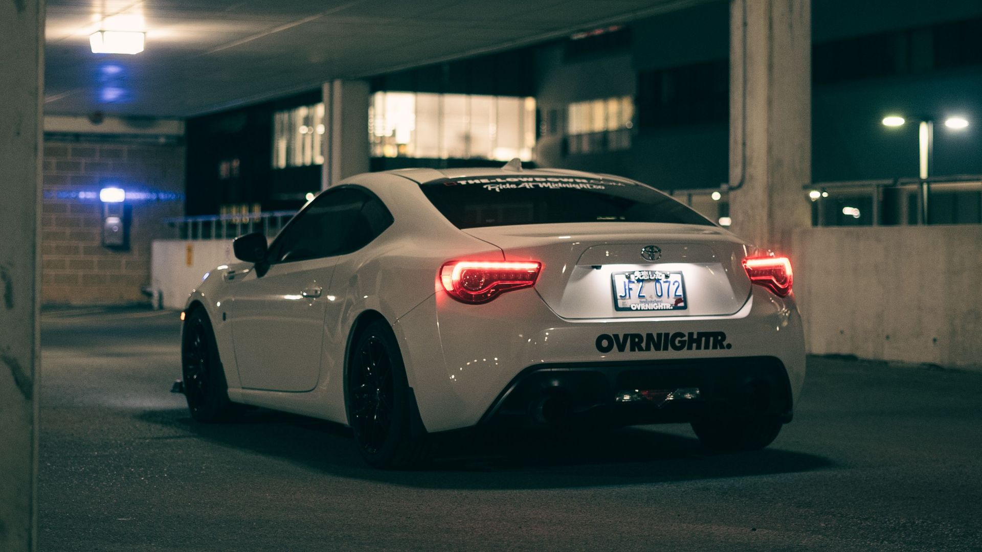 A white sports car parked in a dimly lit urban garage, capturing a modern and moody atmosphere.