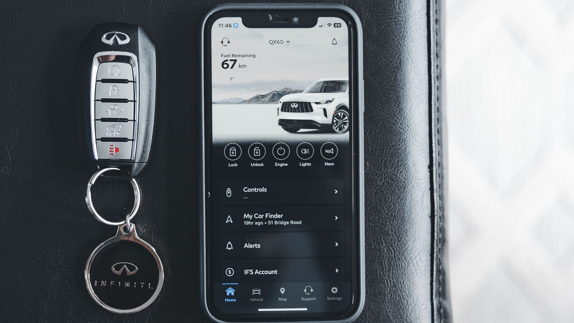 Close-up of an Infiniti key fob and smartphone displaying car app on a leather surface.