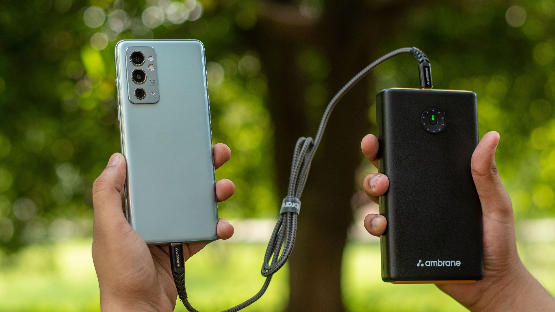 Close-up of hands holding a smartphone connected to a power bank outdoors.