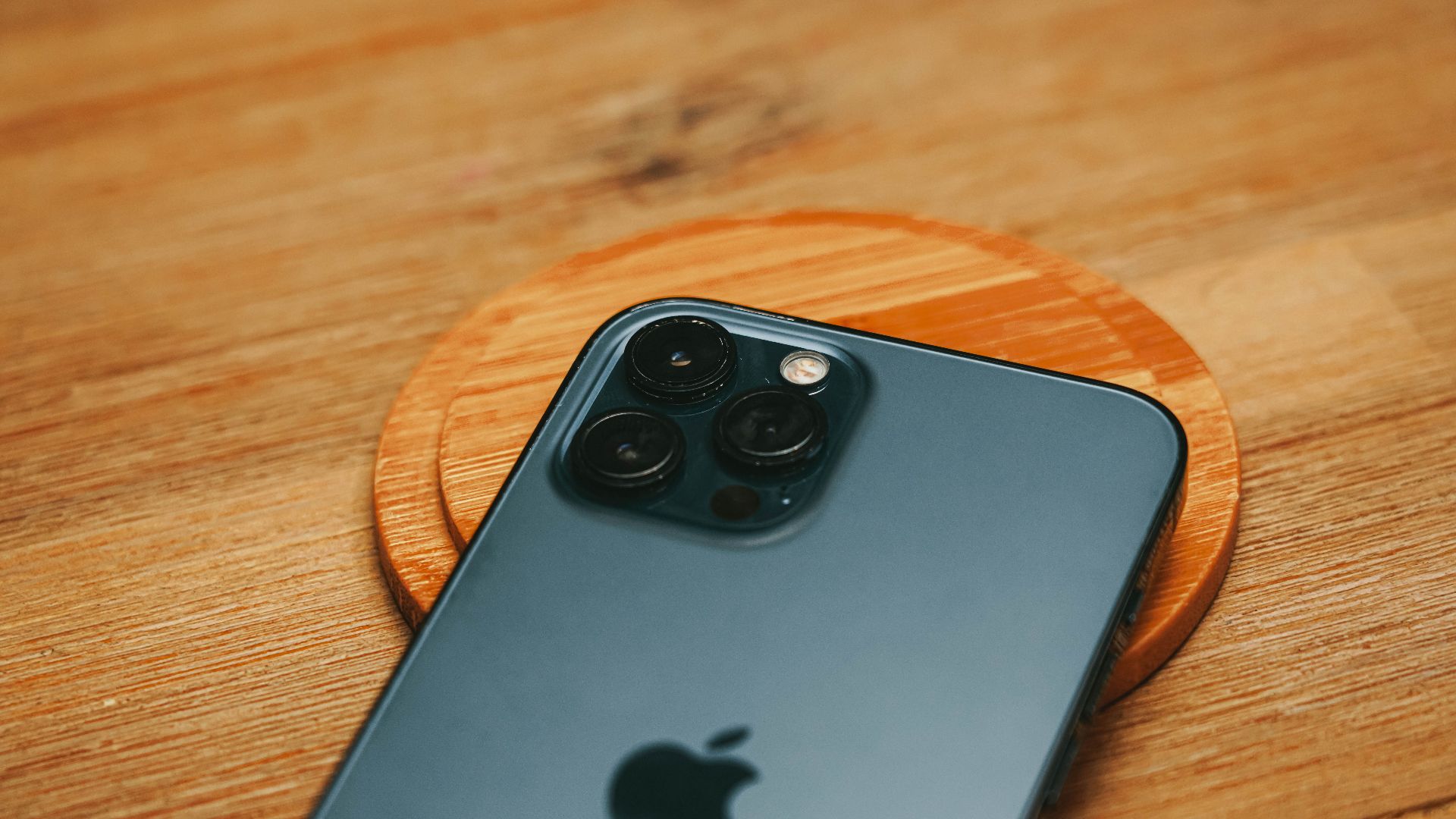 Detailed close-up of a modern smartphone camera on a textured wooden surface.