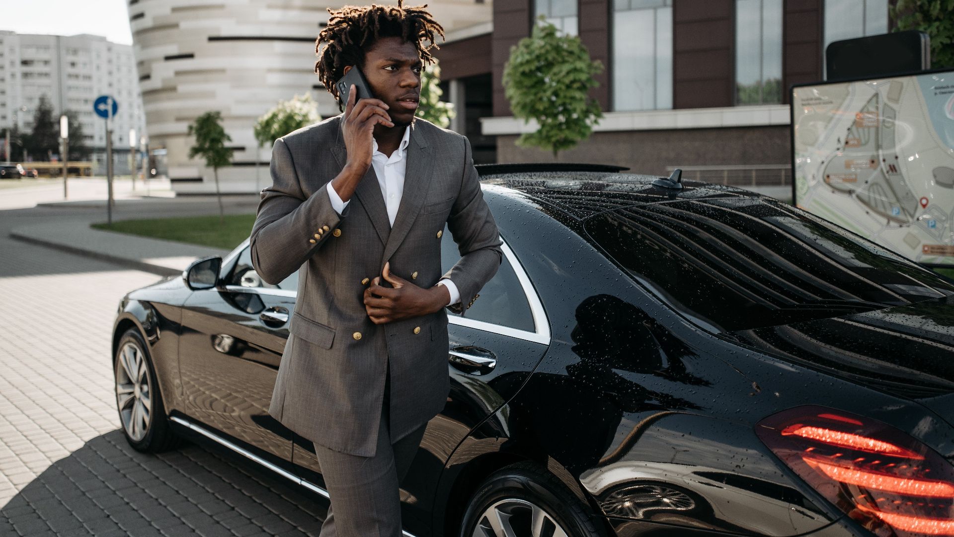 Confident businessman making a phone call while standing beside a luxury black car in an urban setting.