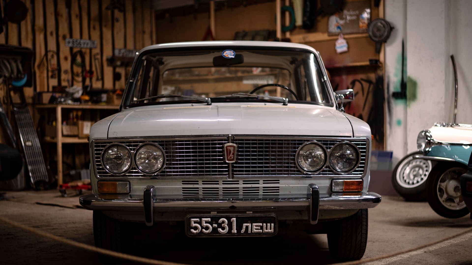 Front view of a vintage VAZ-2103 car parked inside a garage, showcasing its classic design and white livery.